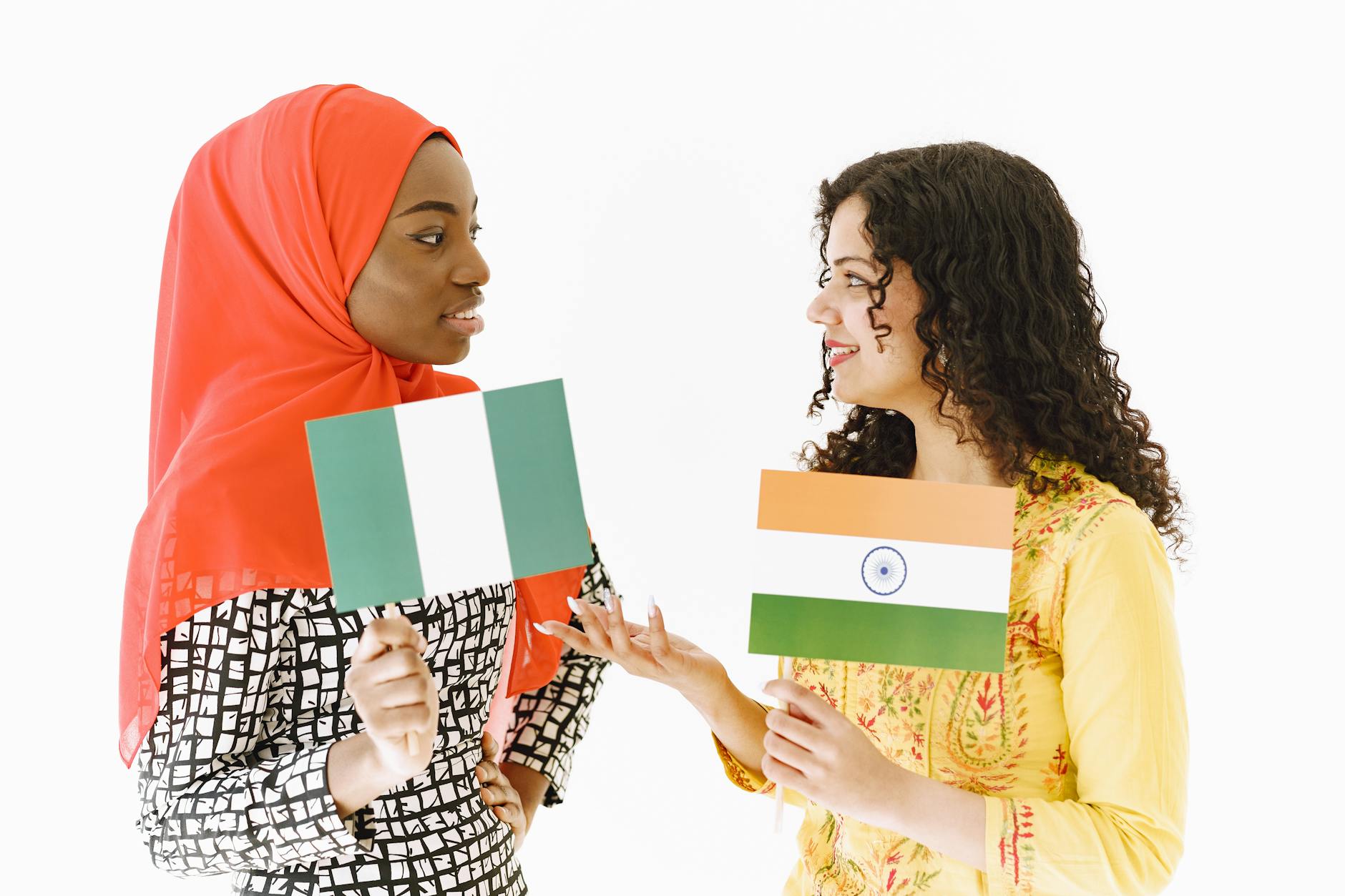 Two women with Nigerian and Indian flags engaging in friendly cultural exchange. - relationship red flags