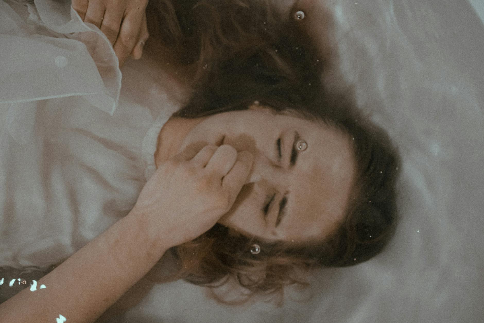 Top view of female with closed eyes and nose lying in clear water in bath - seasonal depression teens