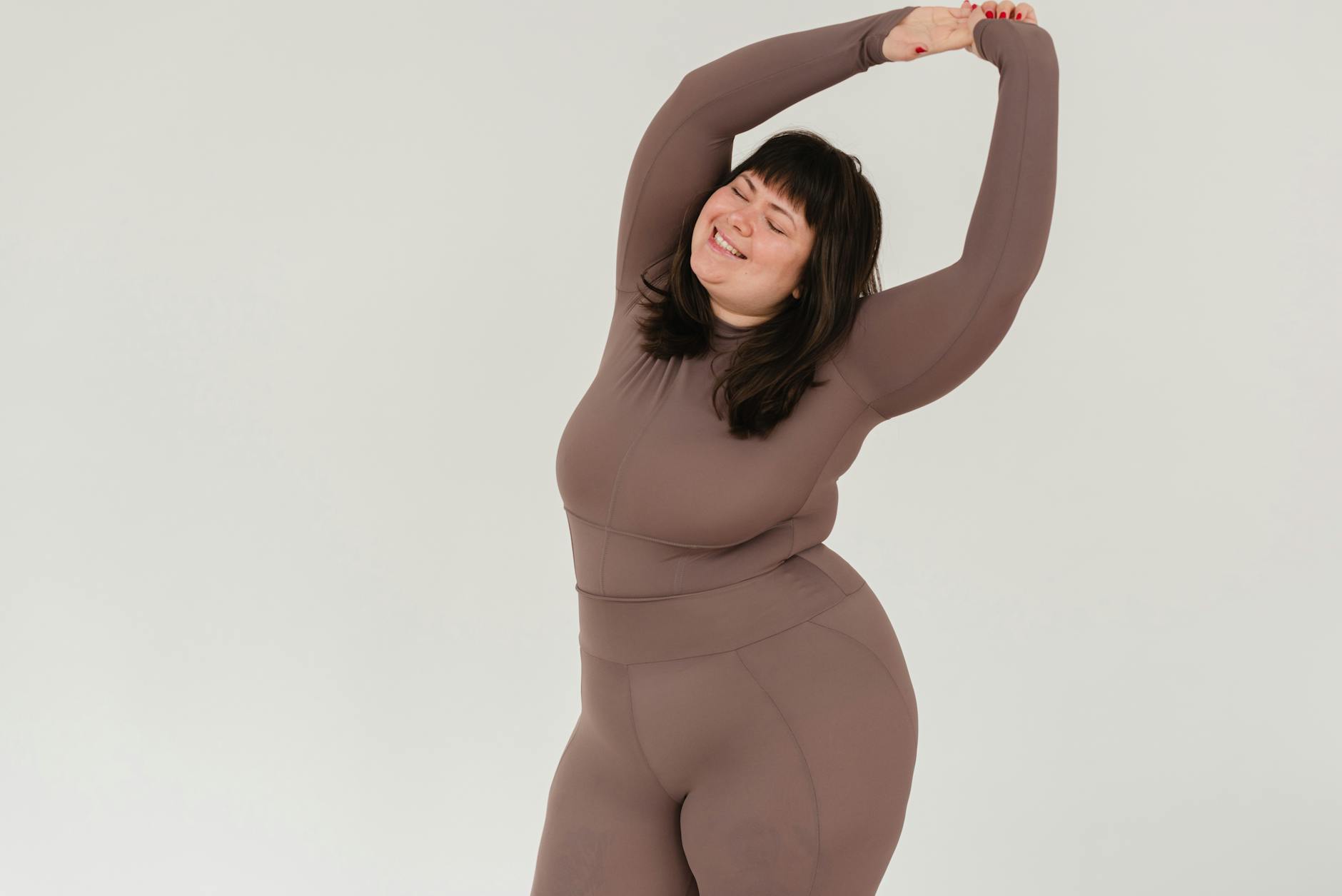 Happy plus-size woman in sportswear stretching confidently in a studio setting. - self esteem building exercises