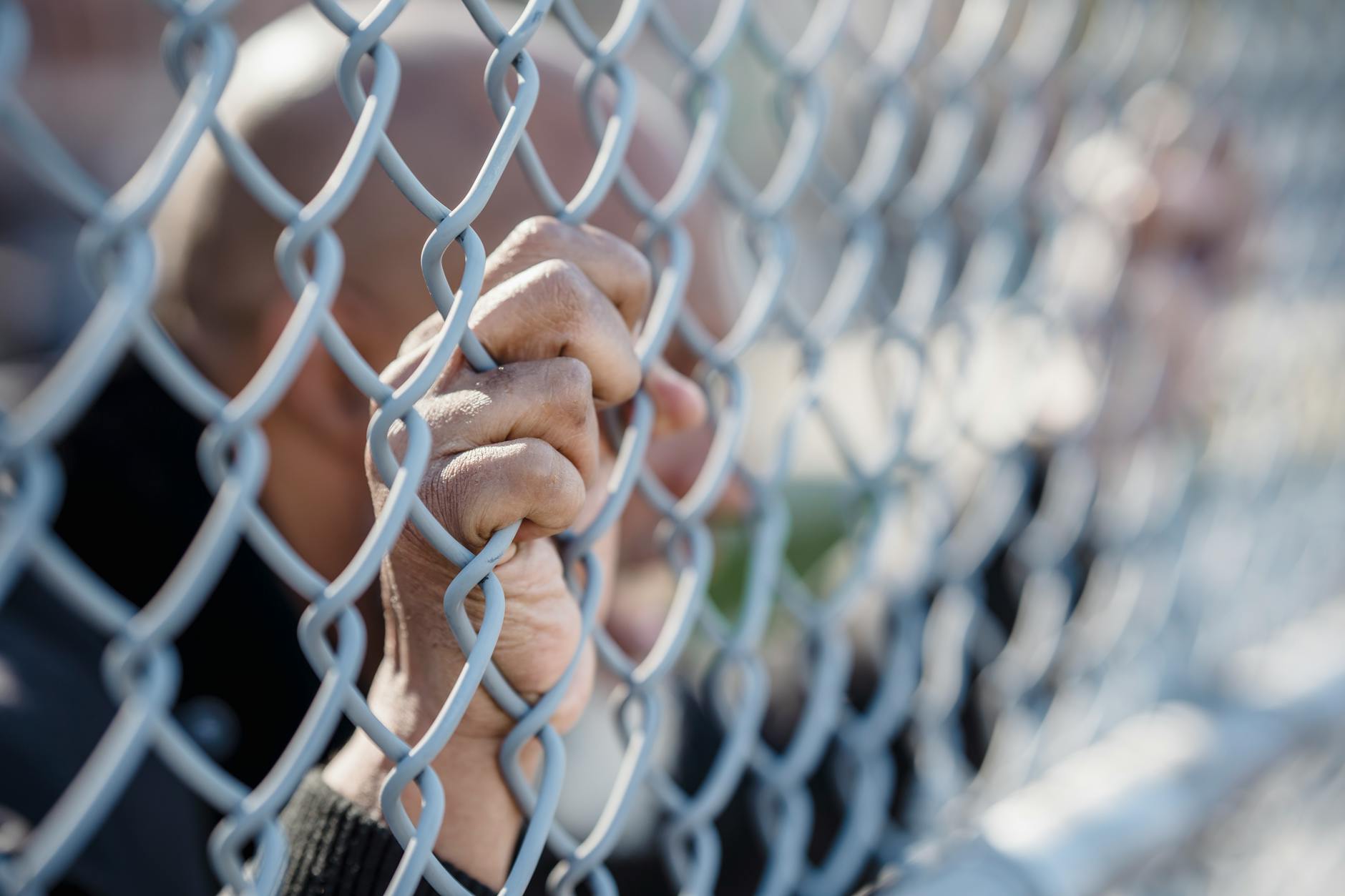 Hands gripping a chain-link fence outdoors, symbolizing confinement or yearning for freedom. - setting boundaries holidays