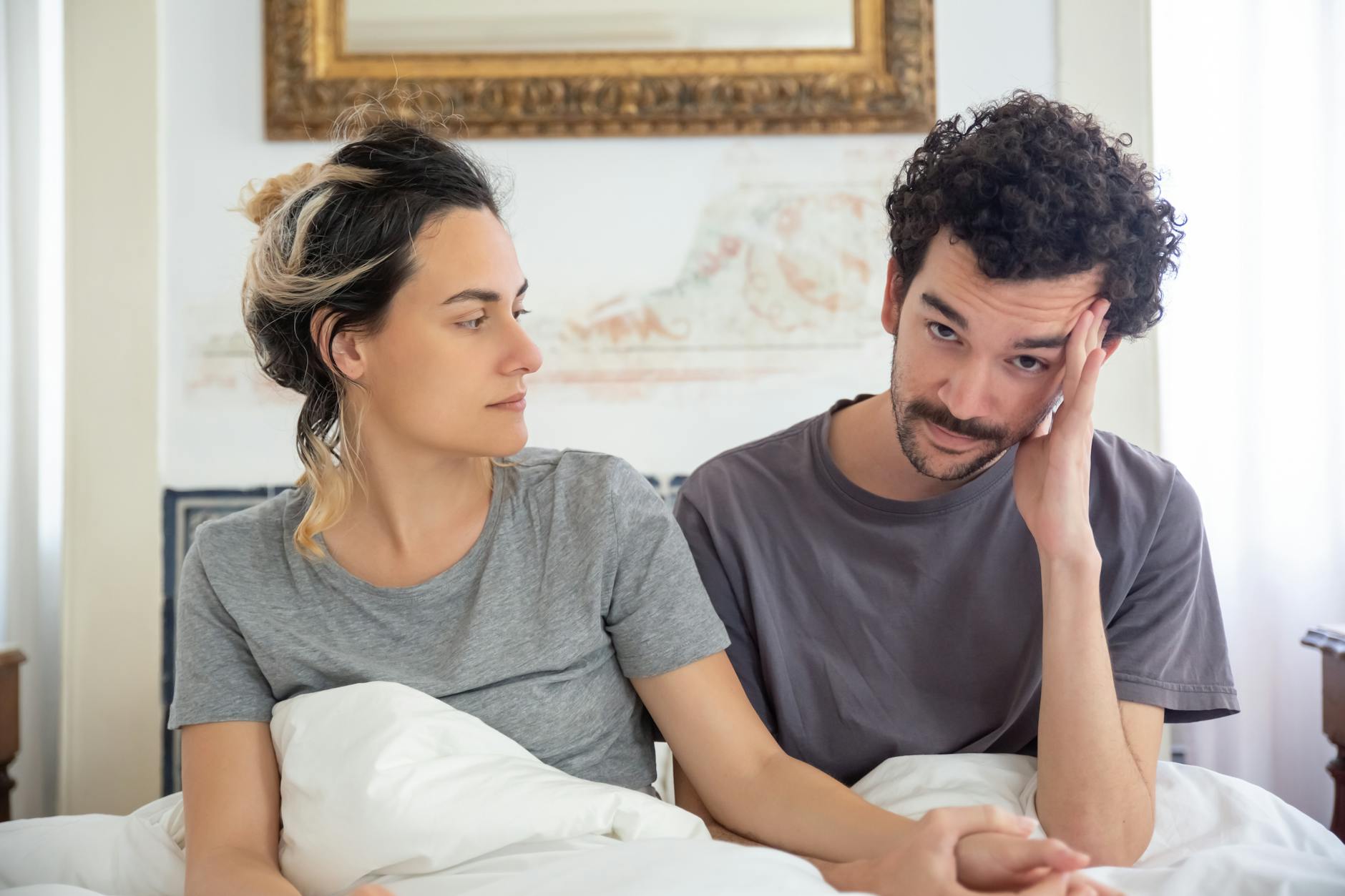 A thoughtful couple seated in bed, sharing an intimate and caring moment at home. - shared relationship goals