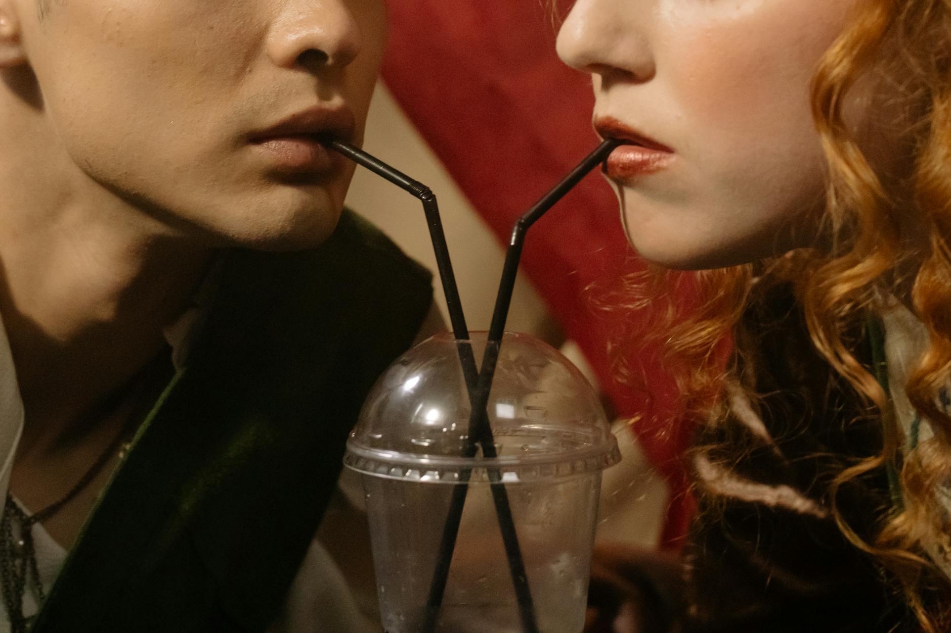 Close-up of a couple sipping from a shared drink with black straws in a plastic cup. - shared relationship goals