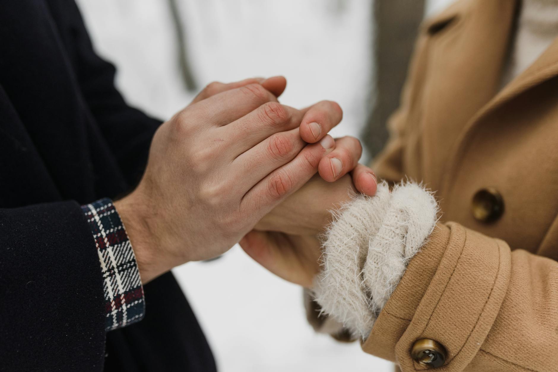 Close-up of a couple's hands holding warmly in a snowy setting, showing affection and connection. - support partner winter blues
