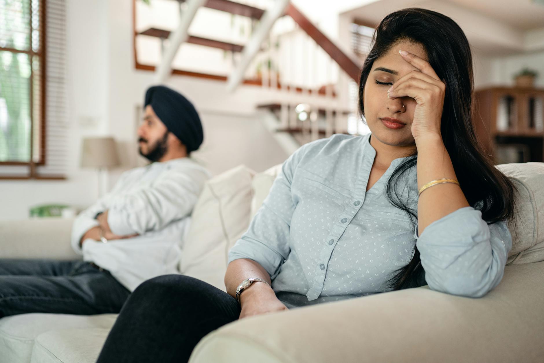 A young couple sitting on a couch indoors, showing signs of stress and frustration. - therapy for commitment issues