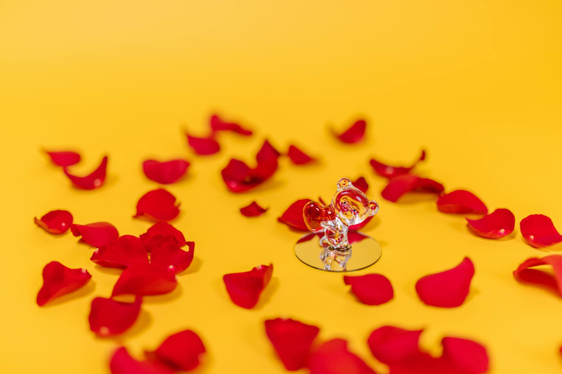 Glass figurine surrounded by red rose petals on a vibrant yellow background, symbolizing love and romance. - valentine's day long distance ideas