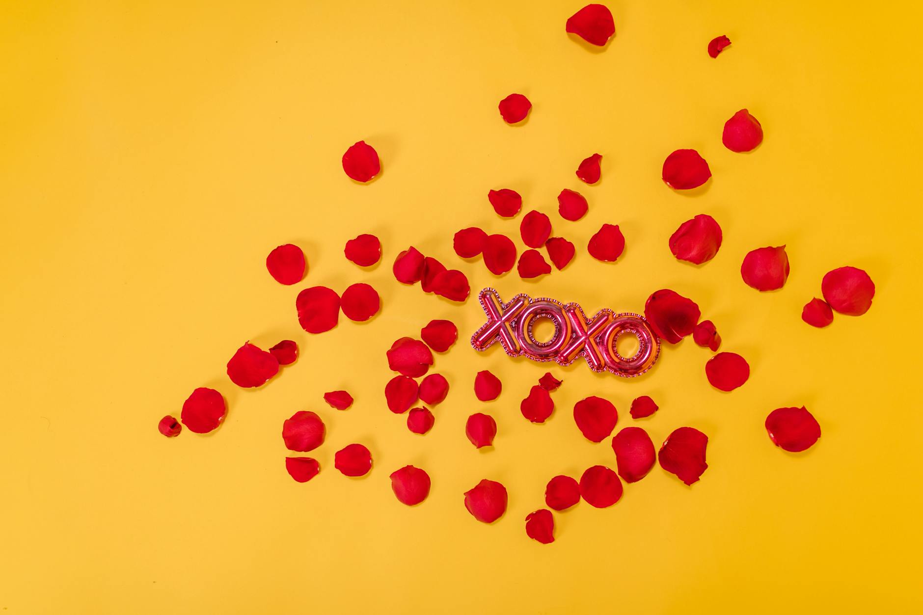 Red rose petals scattered with a XOXO sign on a vibrant yellow background. - valentine's day long distance ideas