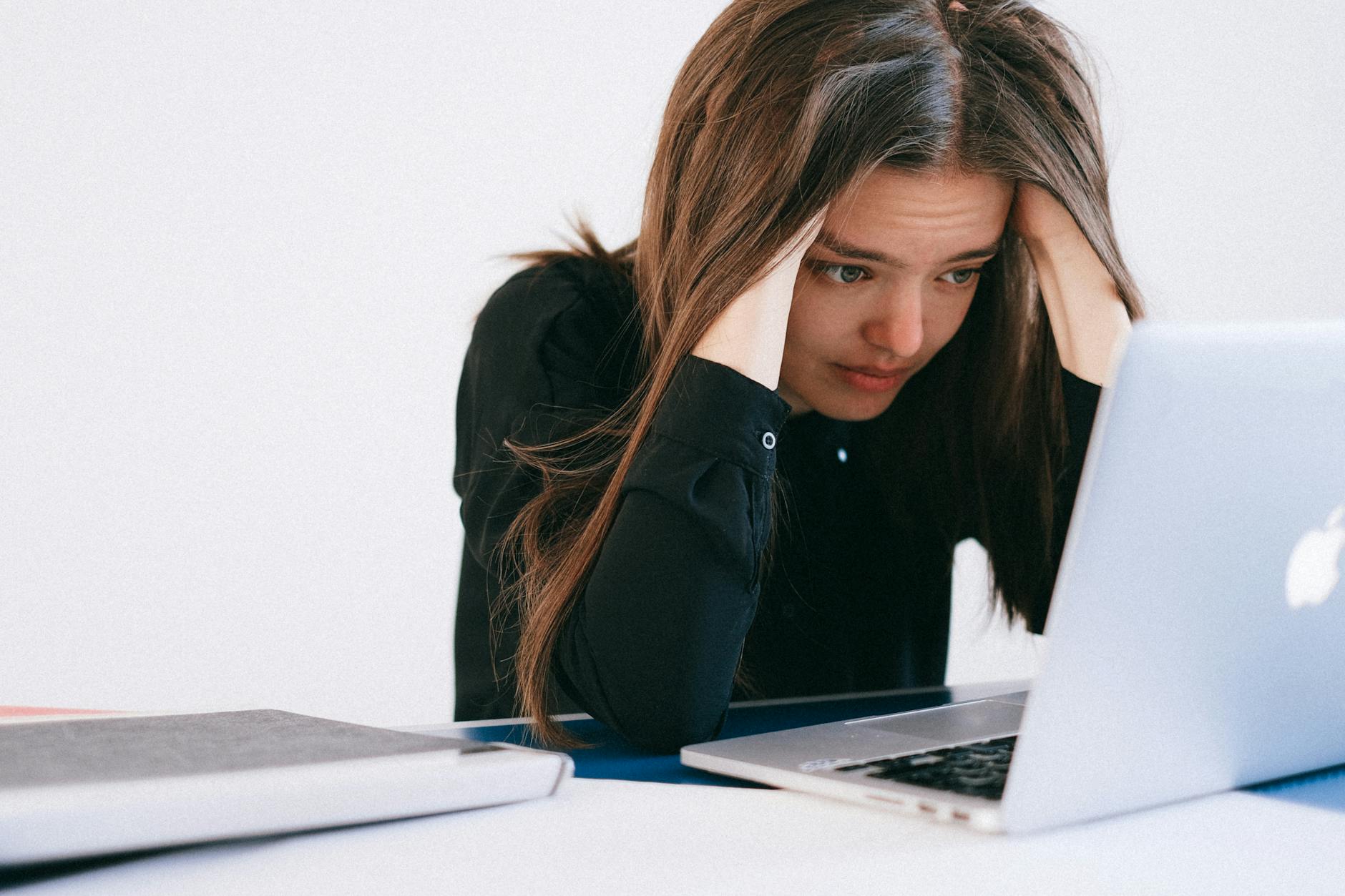 A stressed woman at a desk, looking at a laptop with a worried expression. - winter burnout strategies
