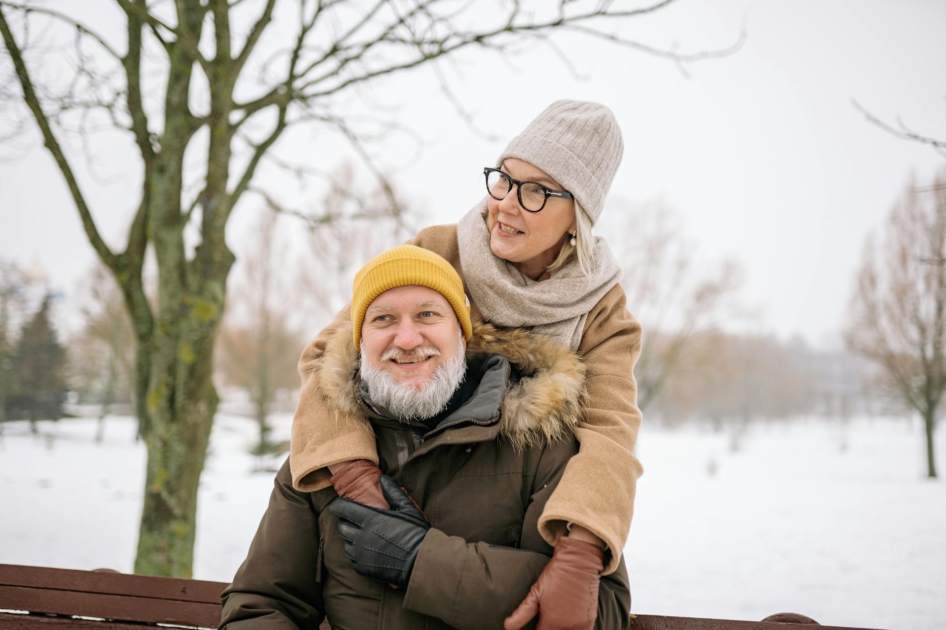 Elderly couple in winter clothes smiling while outdoors in a snowy park. - winter happiness couples