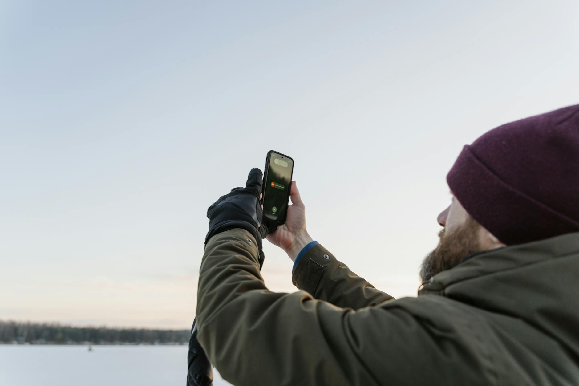 A man in winter clothes using a smartphone outdoors during the daytime. - winter indoor activities no screens