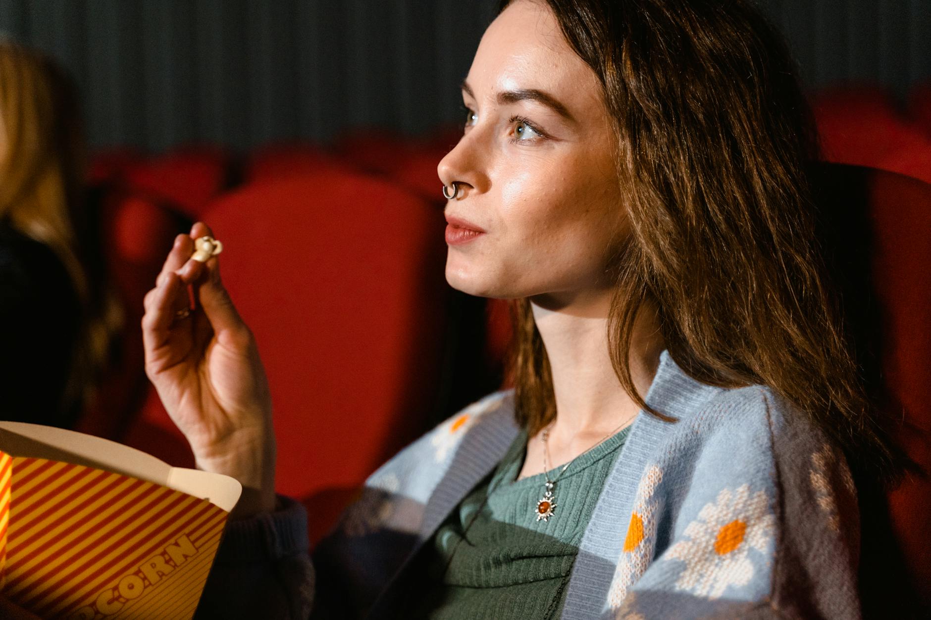A young woman enjoys popcorn while watching a movie in a cinema theater. - winter indoor activities no screens