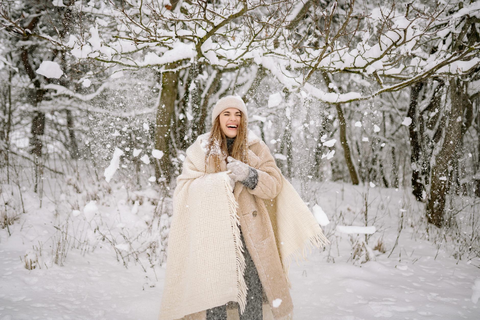 A cheerful woman laughing under snow-covered trees, embodying the winter spirit. - winter mood boost activities