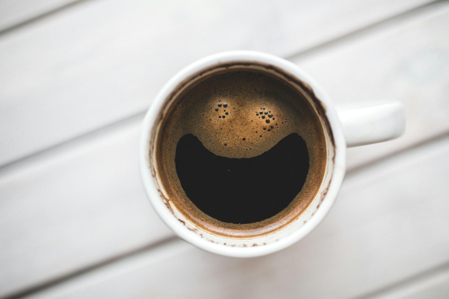 A coffee cup with a smiling face pattern on a wooden table, perfect for morning routines. - winter mood boost activities
