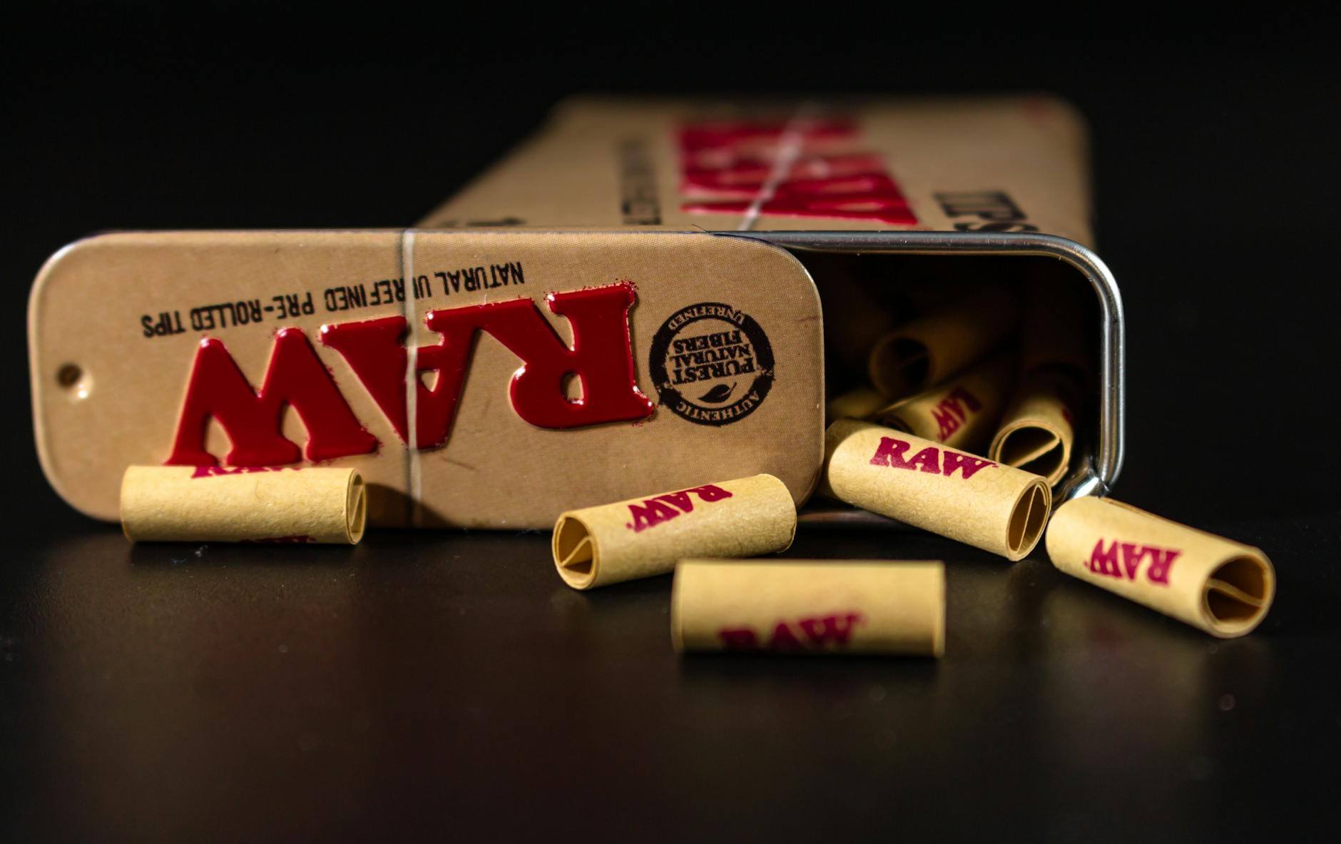 RAW pre-rolled tips spilling from a metal tin on a dark surface, close-up view. - winter mood boosting tips