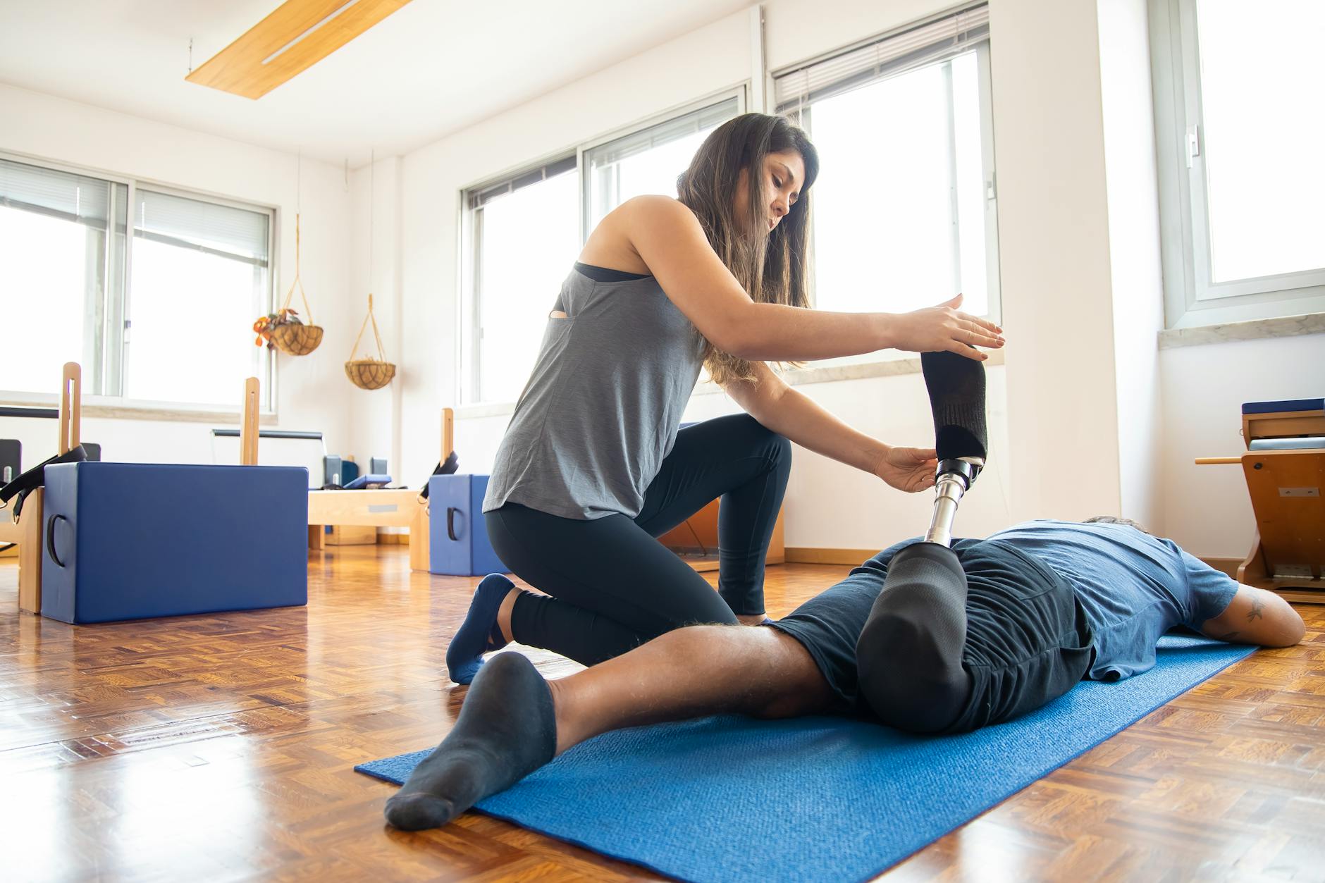 A therapist helps a patient with a prosthetic leg during a rehabilitation session on a yoga mat indoors. - winter therapy motivation