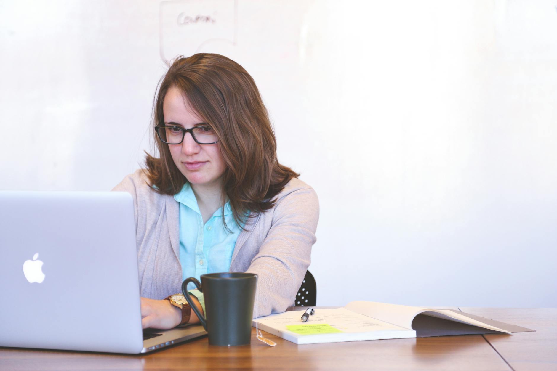 Focused businesswoman using a laptop at a desk with a mug and open notebook. - write apology email