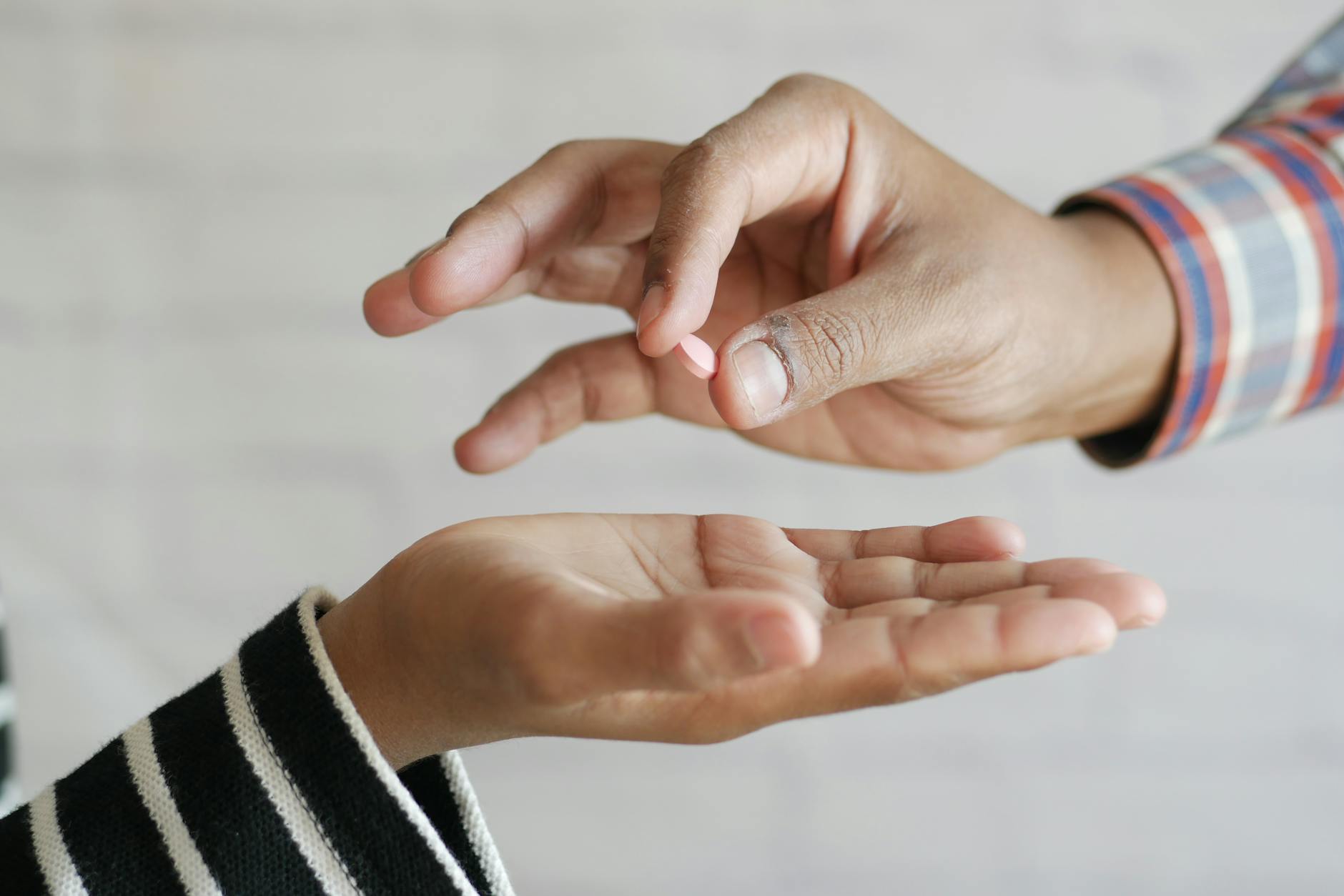Close-up of hands exchanging a single pill, symbolizing medication sharing. - acceptance and commitment therapy spring