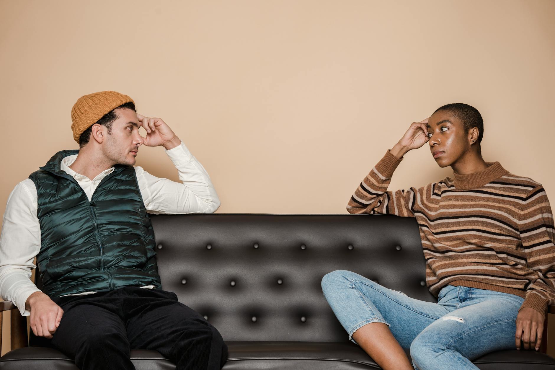 Diverse couple in casual clothes looking at each other with serious faces while sitting on sofa during quarrel in living room - active listening difficult conversations