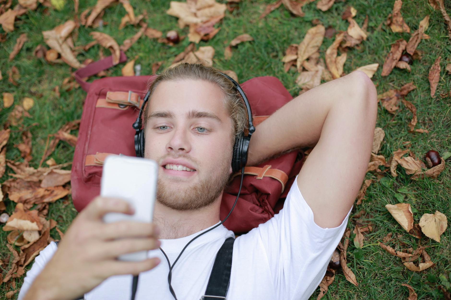 Adult male lying on grass in a park, listening to music with headphones and using a smartphone. - active listening importance