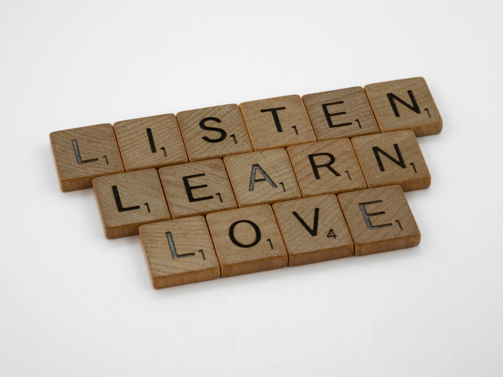 Wooden Scrabble tiles arranged to spell 'Listen, Learn, Love' on a white background. - active listening relationship