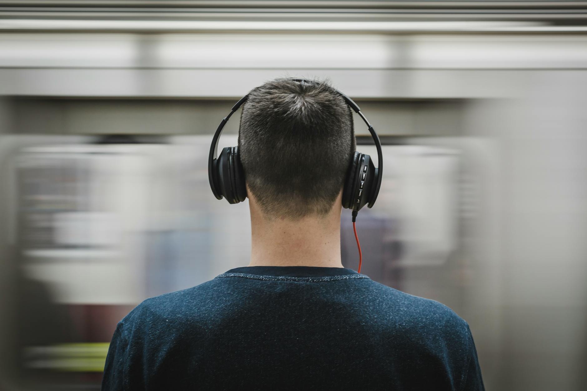 Rear view of a man with headphones standing at a subway platform, blurred train passing by. - active listening relationship