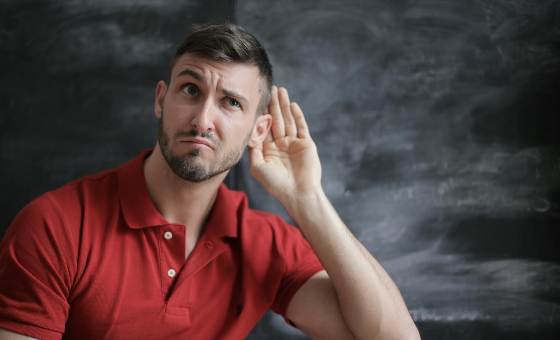 Thoughtful man listening intently against a chalkboard background in a red polo shirt. - active listening steps