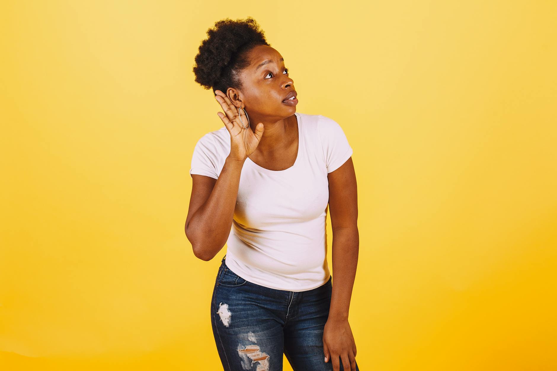 A confident African American woman poses with a listening gesture against a vibrant yellow background. - active listening steps