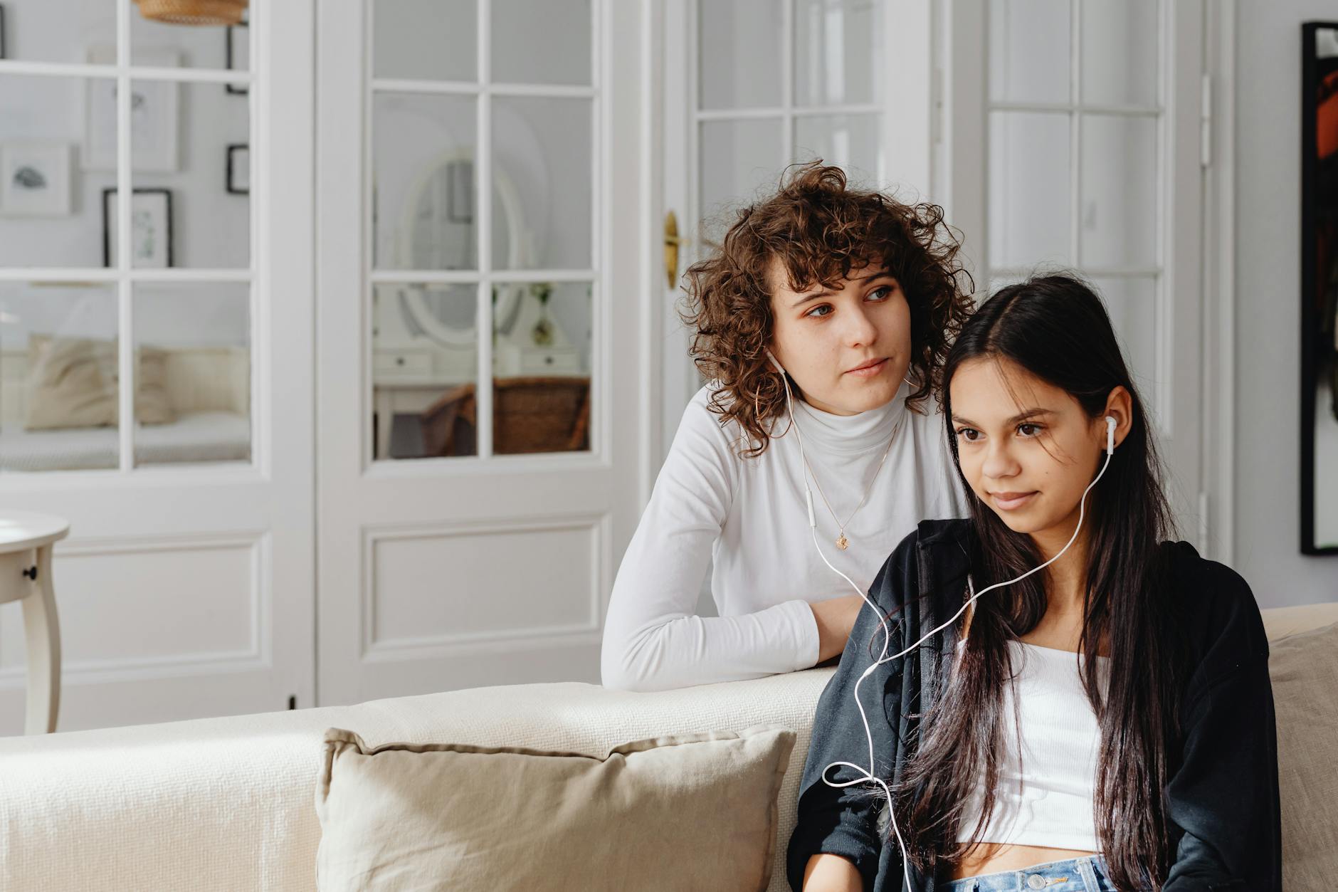 Two women listening to music together with earphones while sitting on a couch indoors. - active listening steps