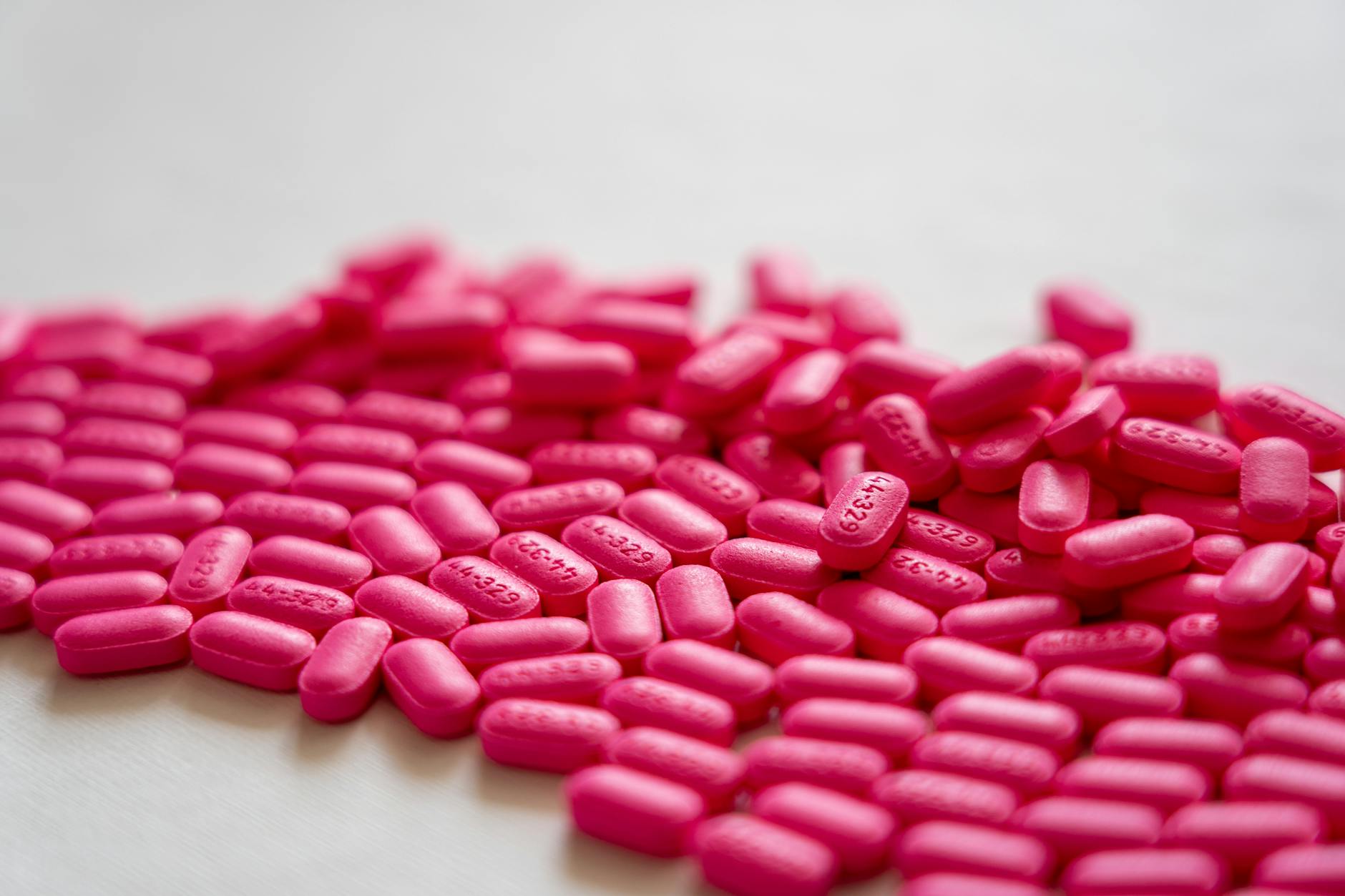 A detailed close-up of vibrant neon pink pills spread on a white table surface. - allergies mood focus