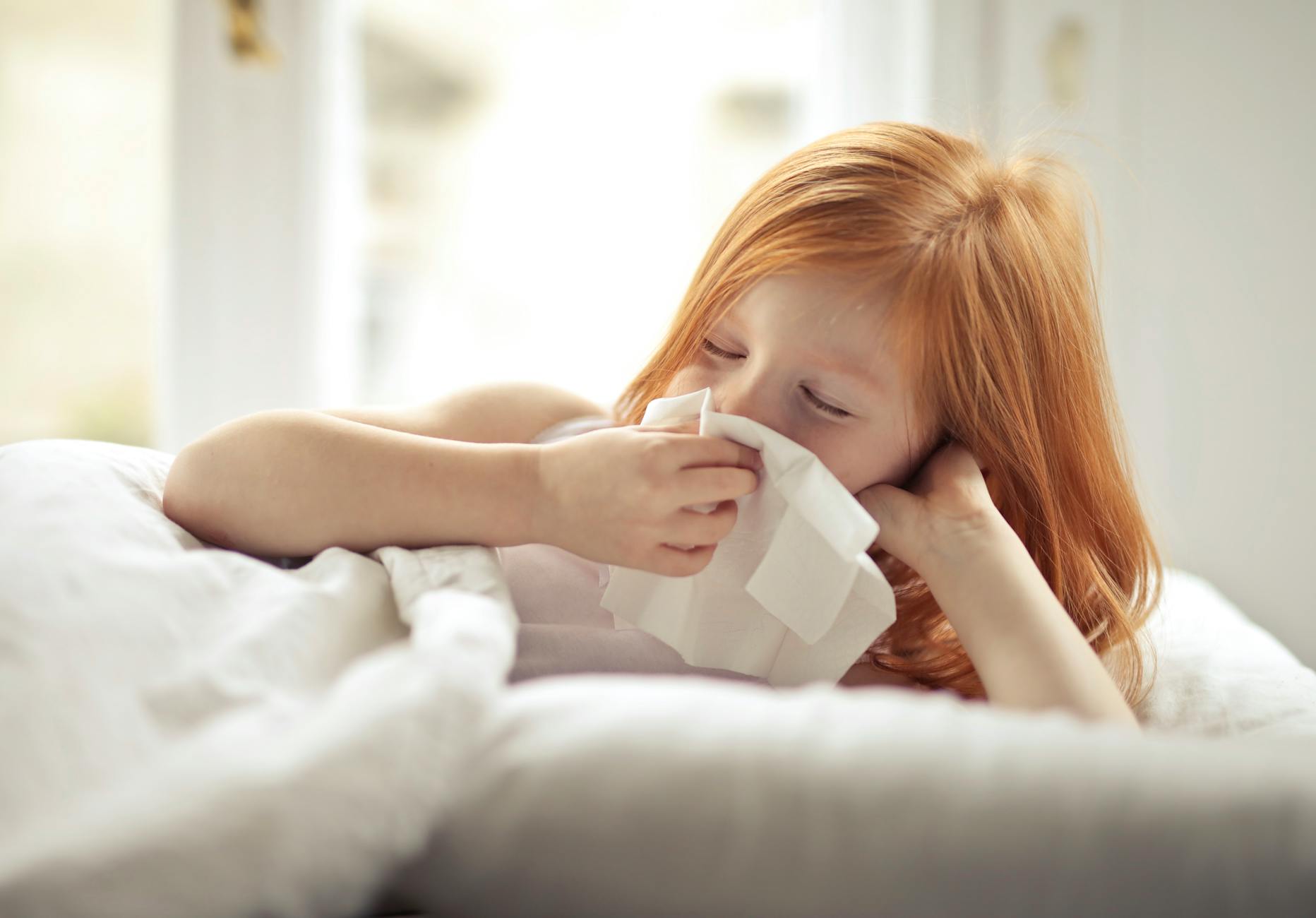 Redheaded child resting in bed, wiping nose with tissue, unwell with flu-like symptoms. - allergy mood changes