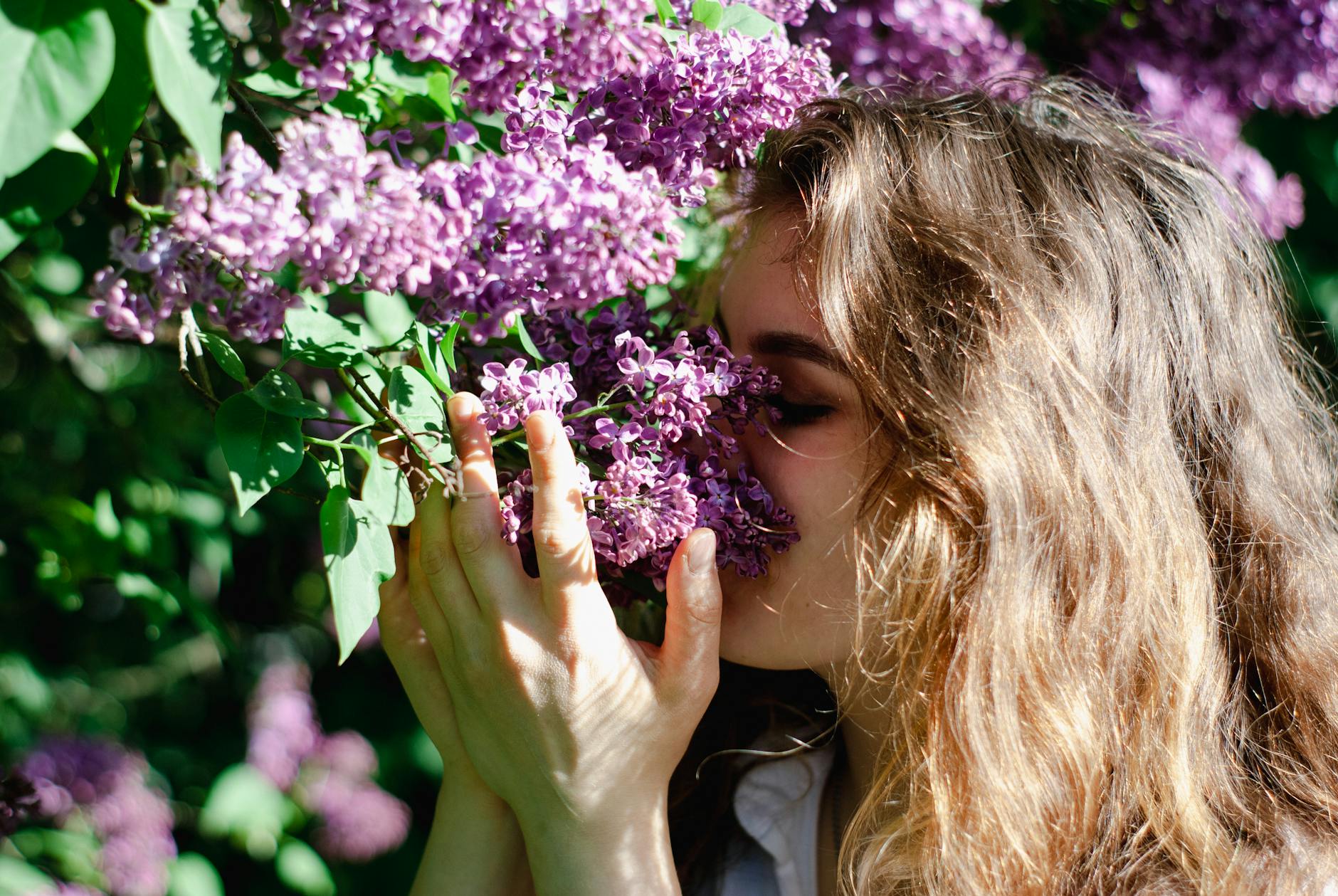 A young woman relishes the scent of lilac flowers in a sunlit garden, embodying spring and relaxation. - allergy mood therapy