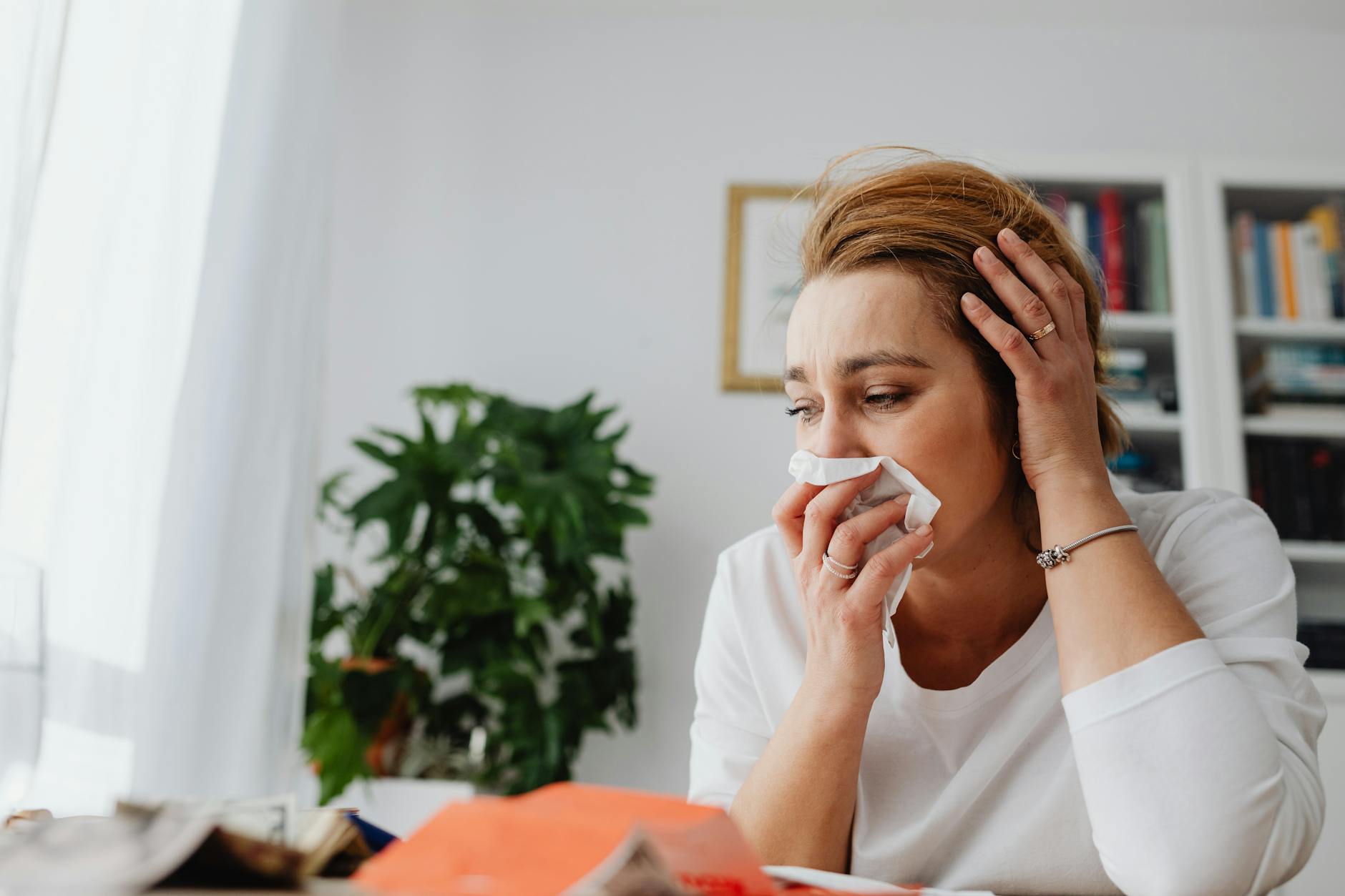 An adult woman feeling unwell, blowing her nose indoors. - allergy mood therapy