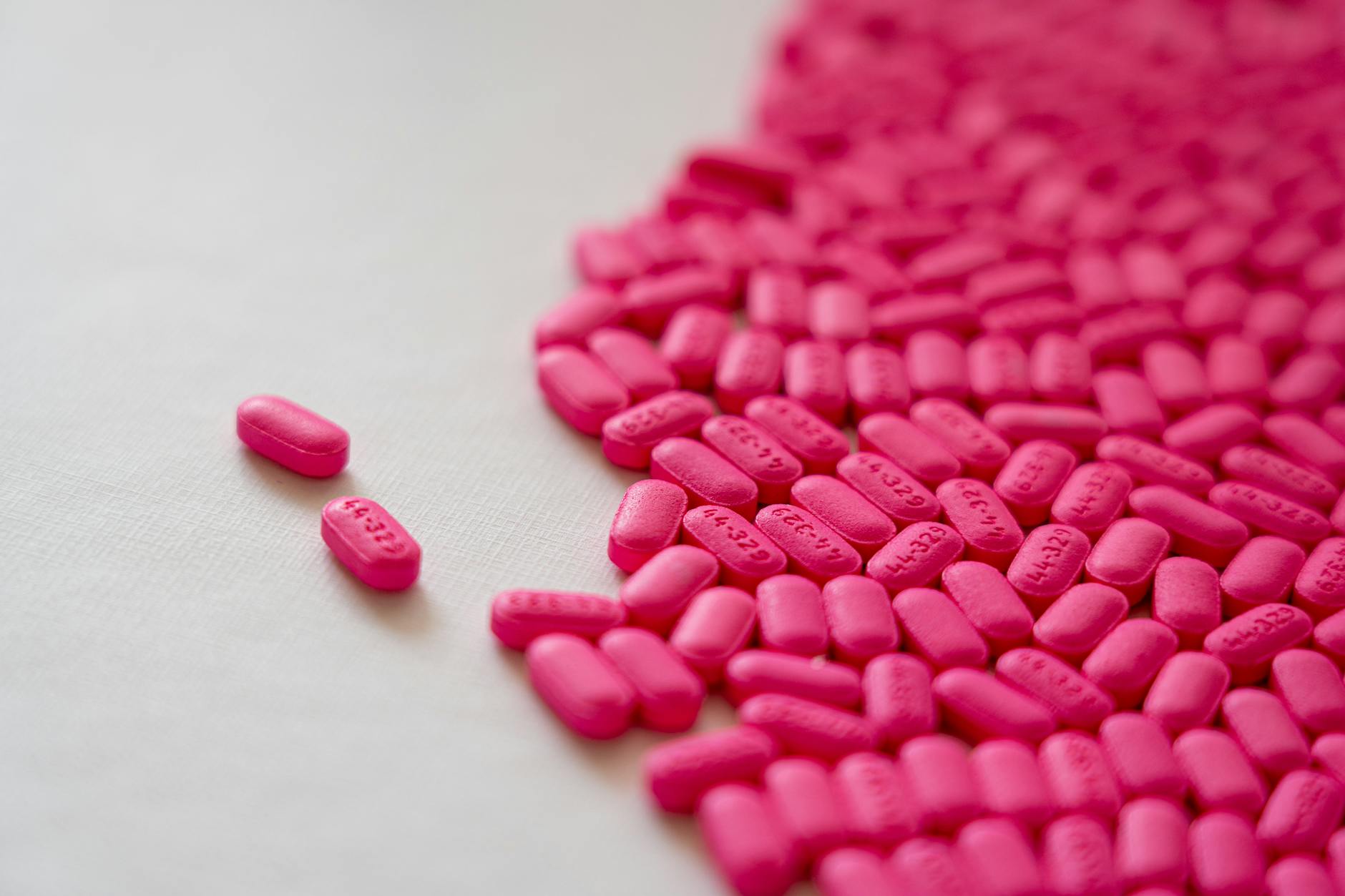 Close-up of bright pink pills scattered on a white surface, emphasizing healthcare and medication theme. - allergy relationship strain