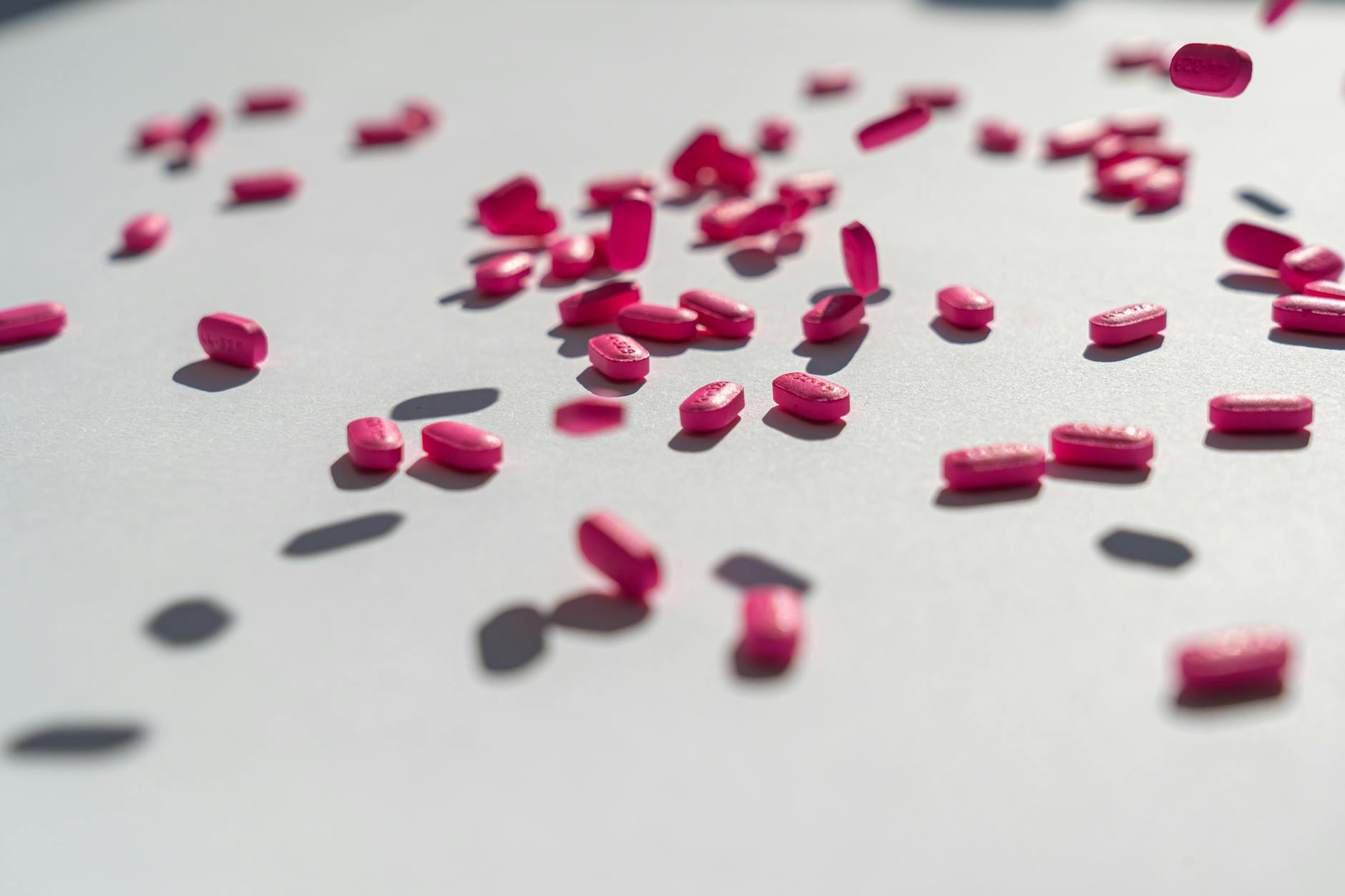 Close-up view of neon pink pills scattered on a white surface with dramatic shadows, depicting medication concepts. - allergy relationship strain