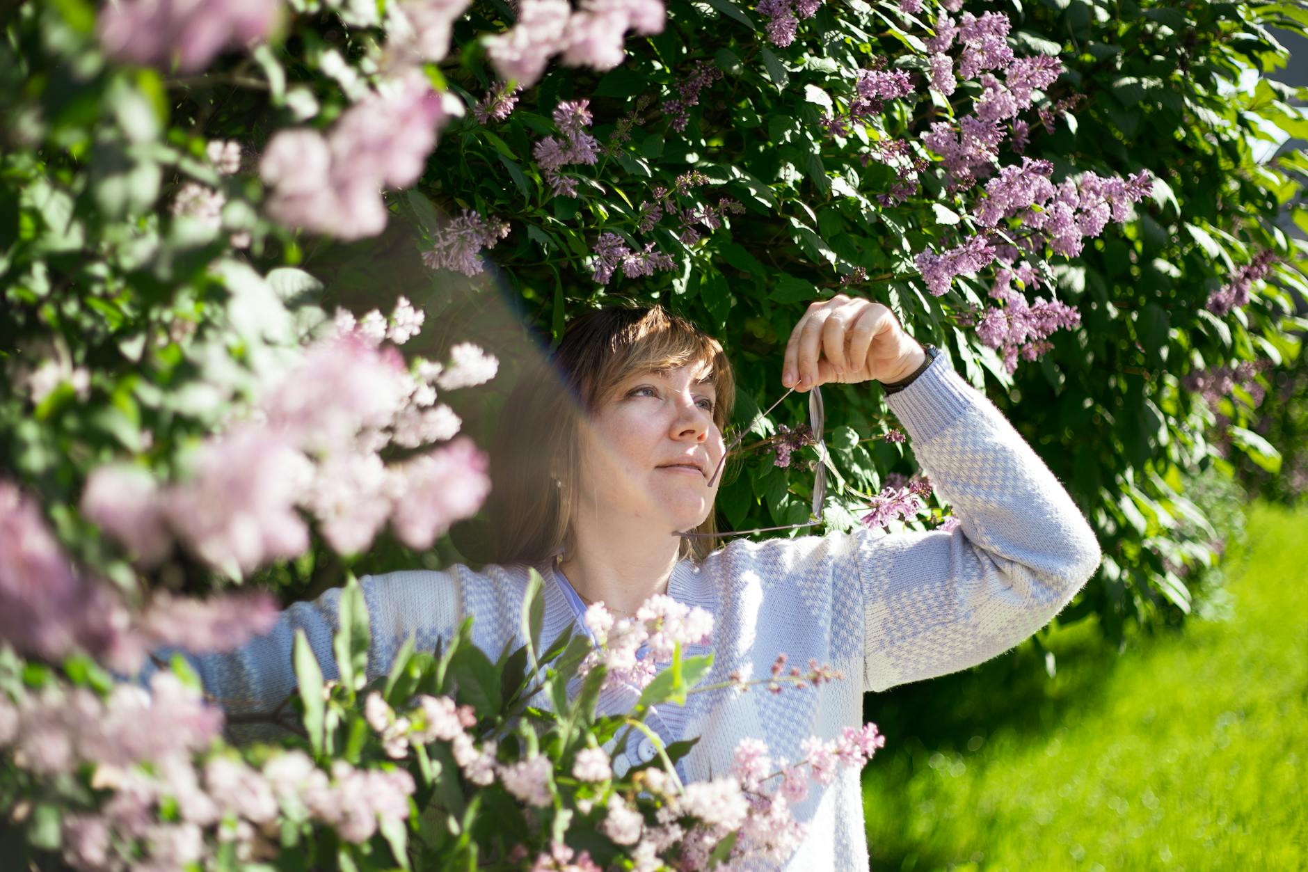 A woman appreciating the beauty of lilac blossoms in a sunny spring garden. - allergy season relationship