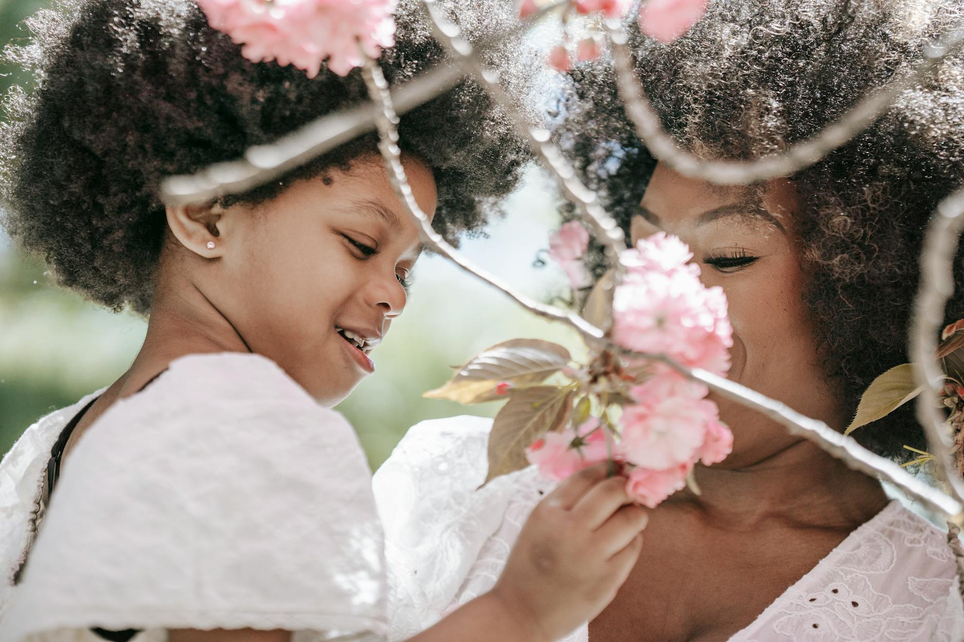 A mother and daughter share a joyful moment surrounded by blooming cherry blossoms outdoors. - allergy season relationship
