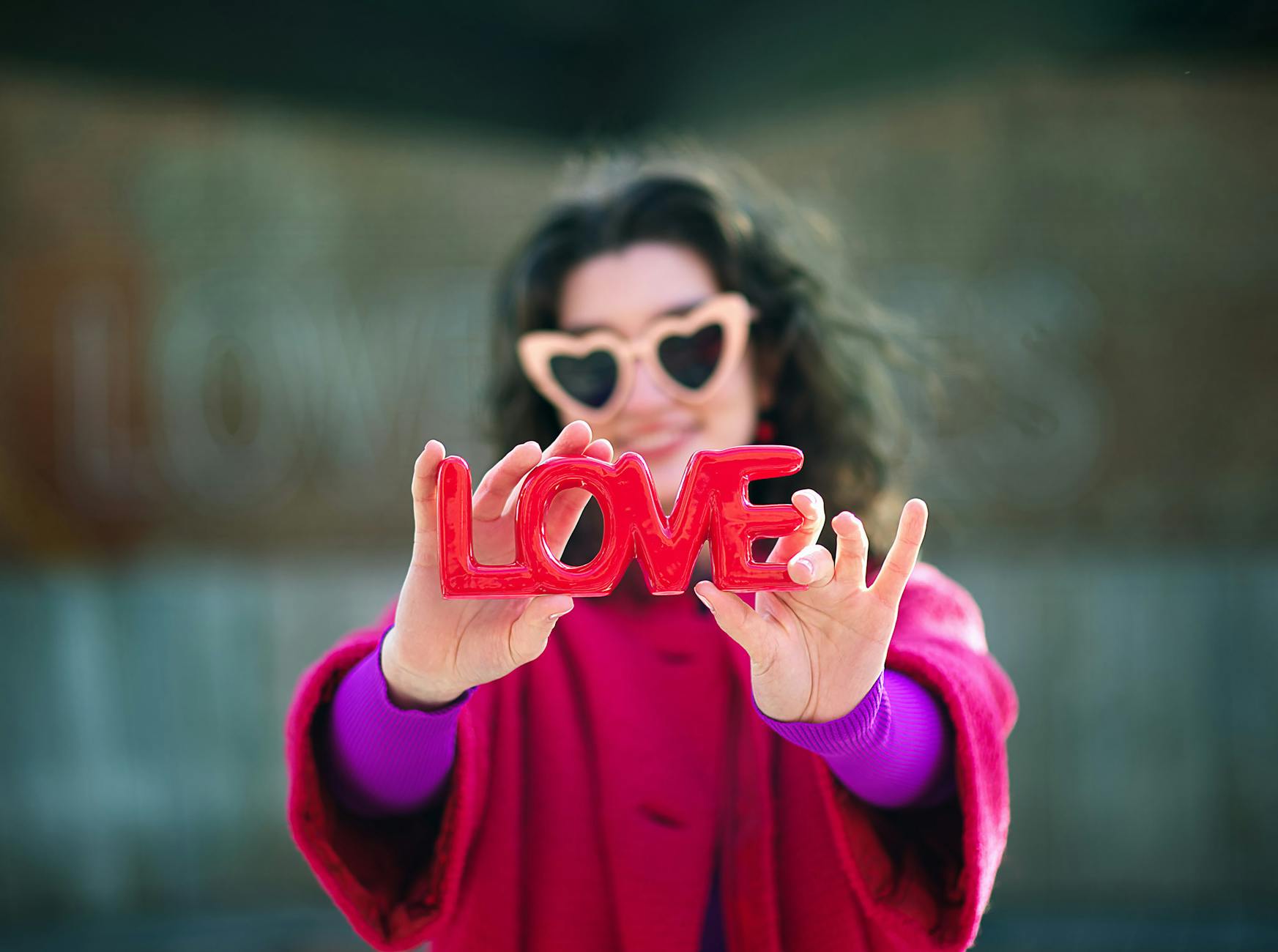 A smiling young woman with heart-shaped sunglasses holding a bright red LOVE sign. Outdoor setting, vibrant colors. - how to apologize