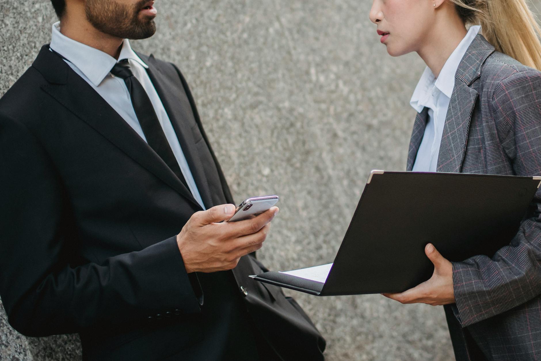 Business professionals in formal wear discussing while holding a laptop and phone. - assertive communication examples