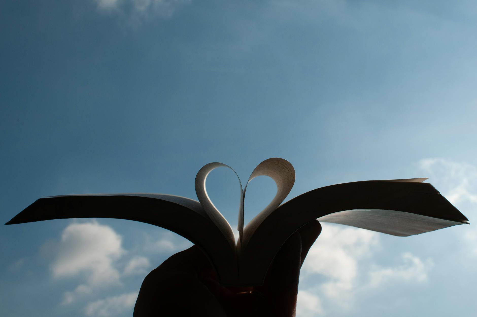 A heart shape formed by an open book's pages with a clear blue sky background in Milano, Italy. - assertive communication meaning