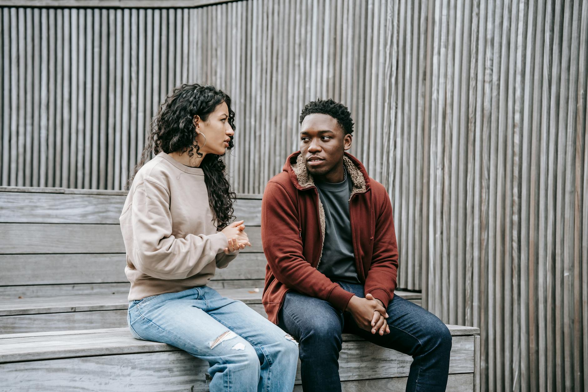 A couple having a serious conversation while sitting on outdoor wooden stairs. - assertive communication skills
