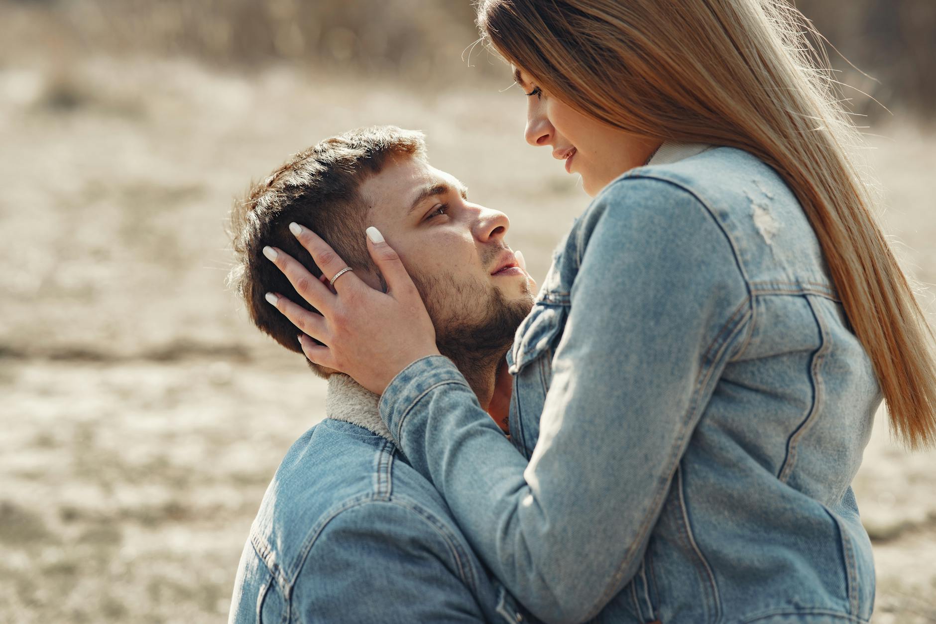 Side view of loving young couple in denim jackets hugging and looking at each other while spending time together on grassy meadow in countryside - attachment style quiz