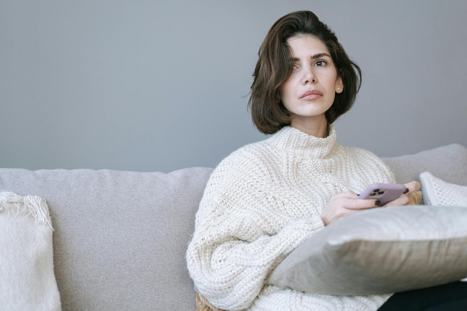 A thoughtful woman in a cozy sweater relaxing on a sofa while using her smartphone indoors. - avoidant attachment style