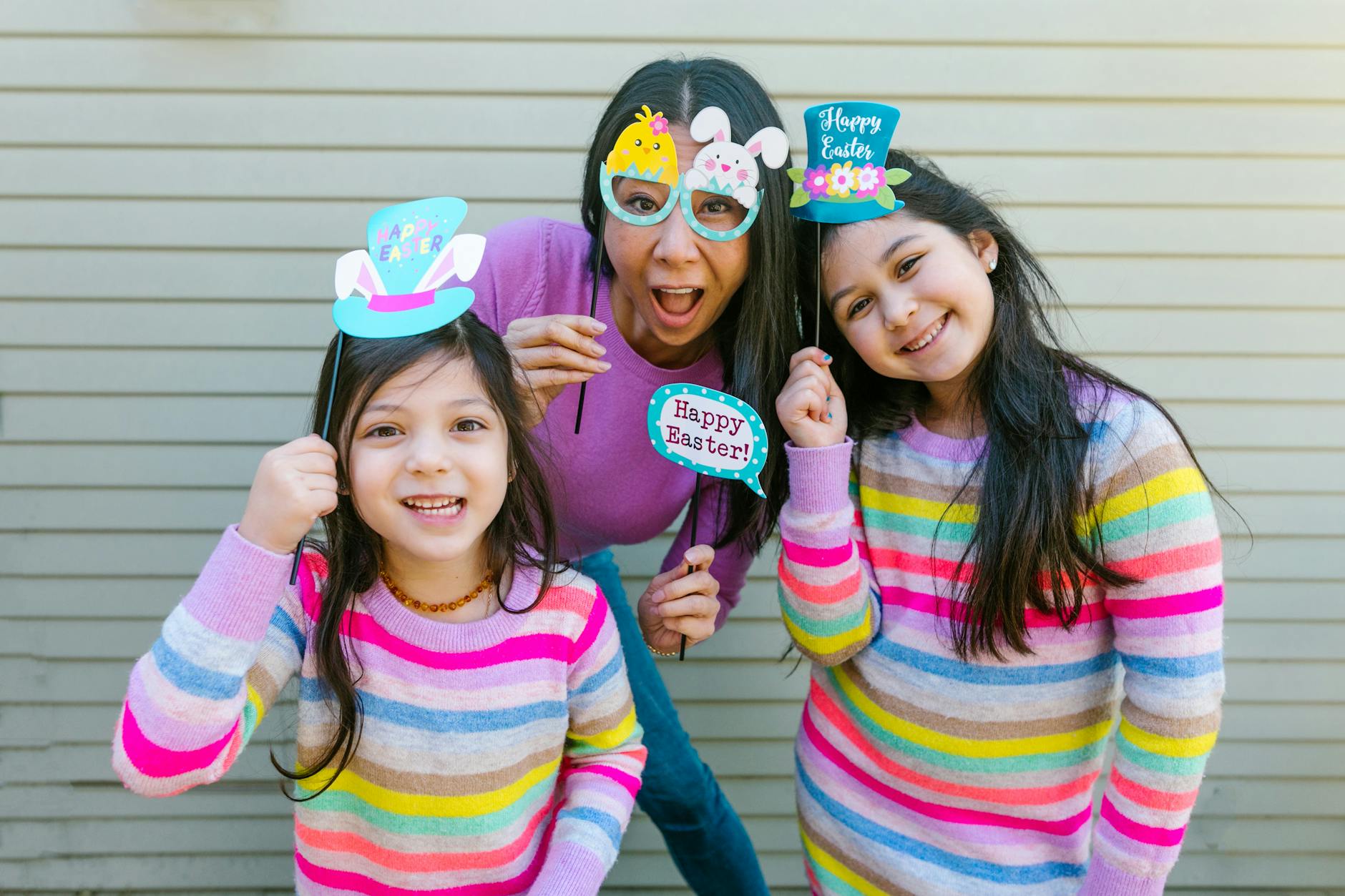 A mother and her daughters celebrate Easter with fun props and colorful sweaters, showcasing festive spirit. - blended family spring holidays