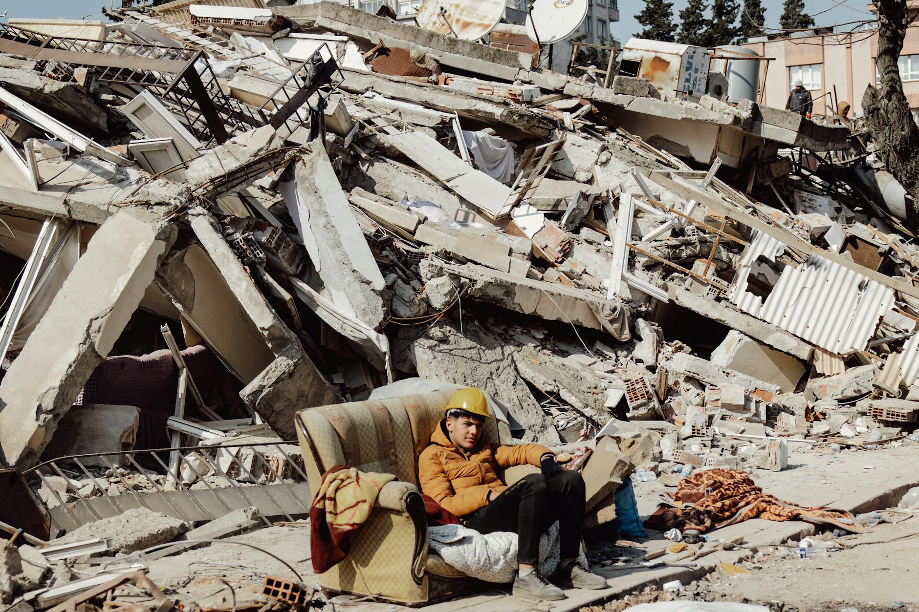 Young man in helmet on a sofa surrounded by destroyed buildings after earthquake. - build resilience