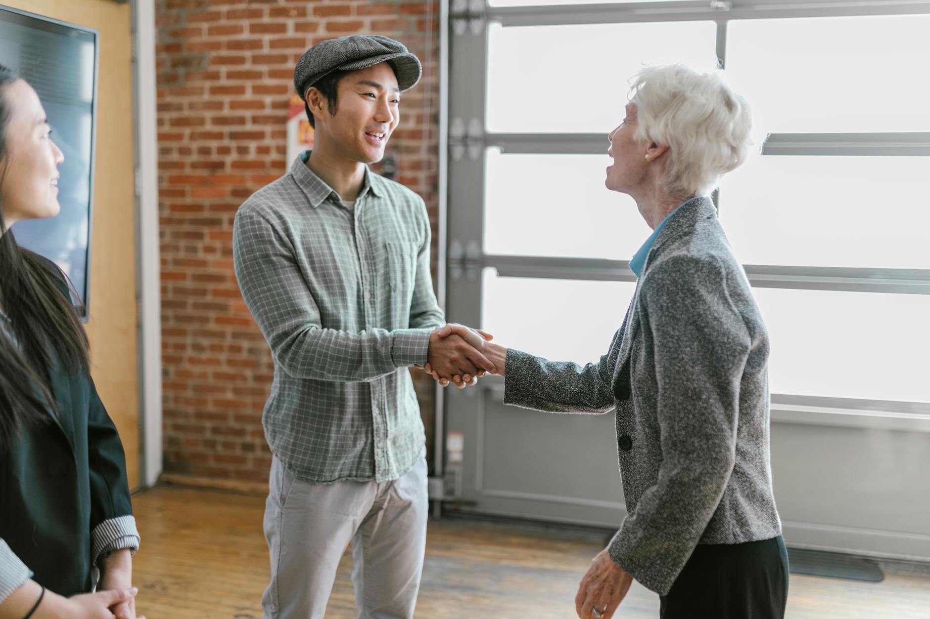 Young man and elderly woman shaking hands in a modern office setting. - build trust relationships