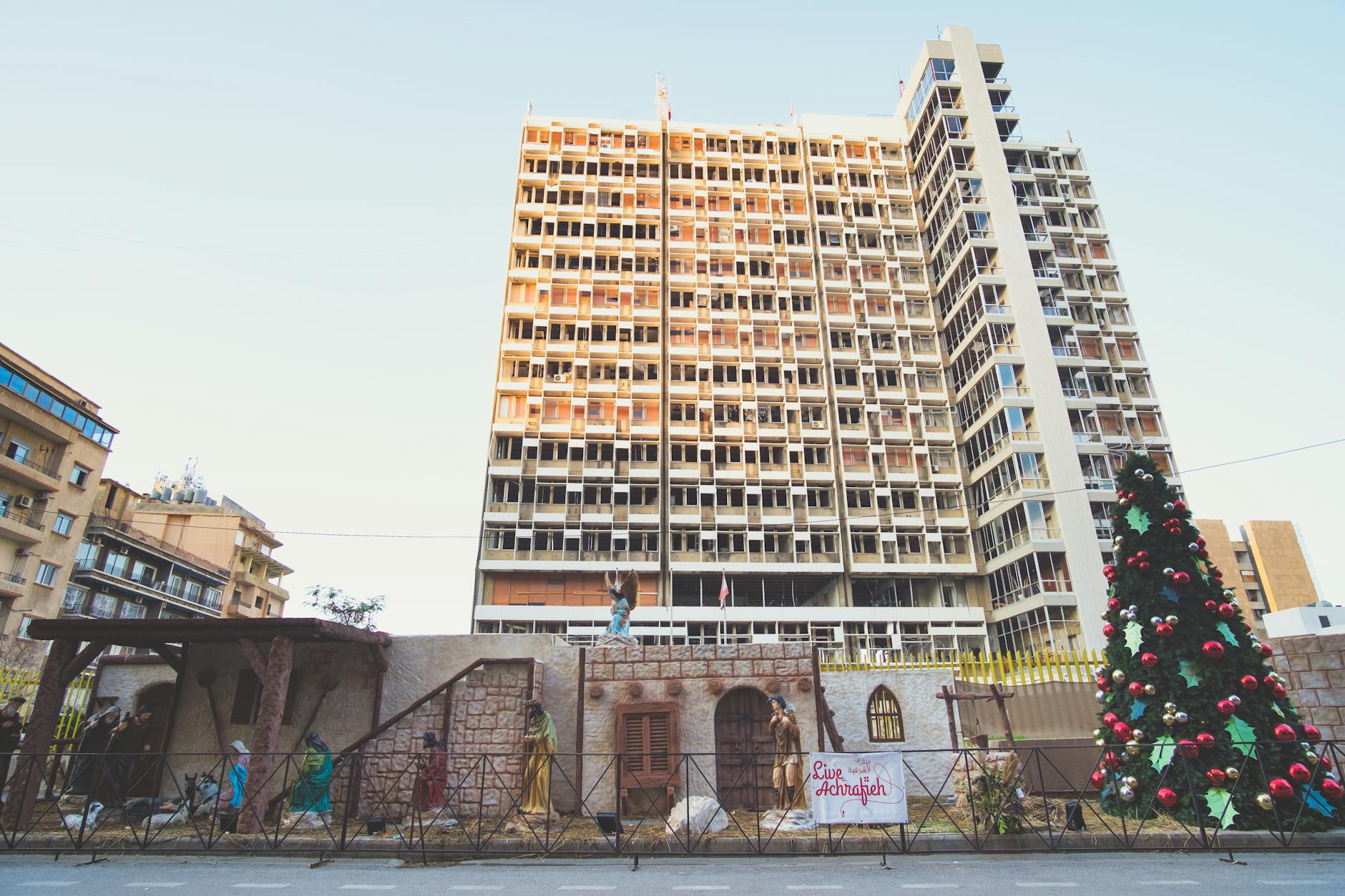 Urban scene in Beirut showcasing a Christmas tree beside a damaged building, reflecting resilience. - building resilience
