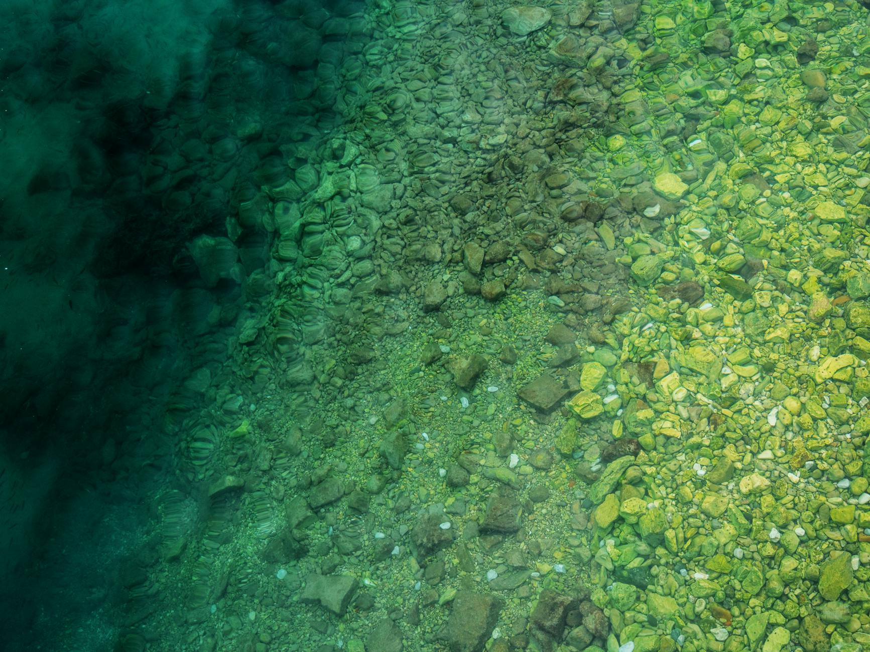 A mesmerizing aerial capture of a clear shoreline with visible pebbles and stones in vibrant green waters. - cbt for clarity