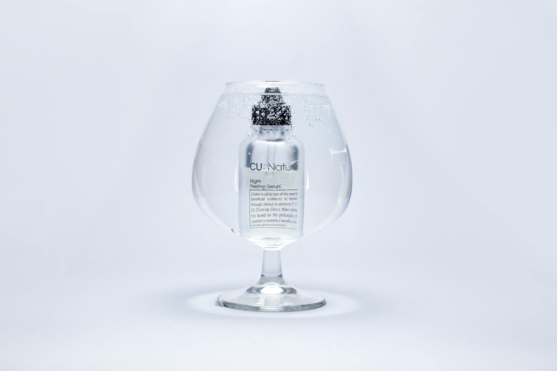 A luxury serum bottle submerged in a large wine glass filled with water, showcasing purity and elegance. - cbt for clarity