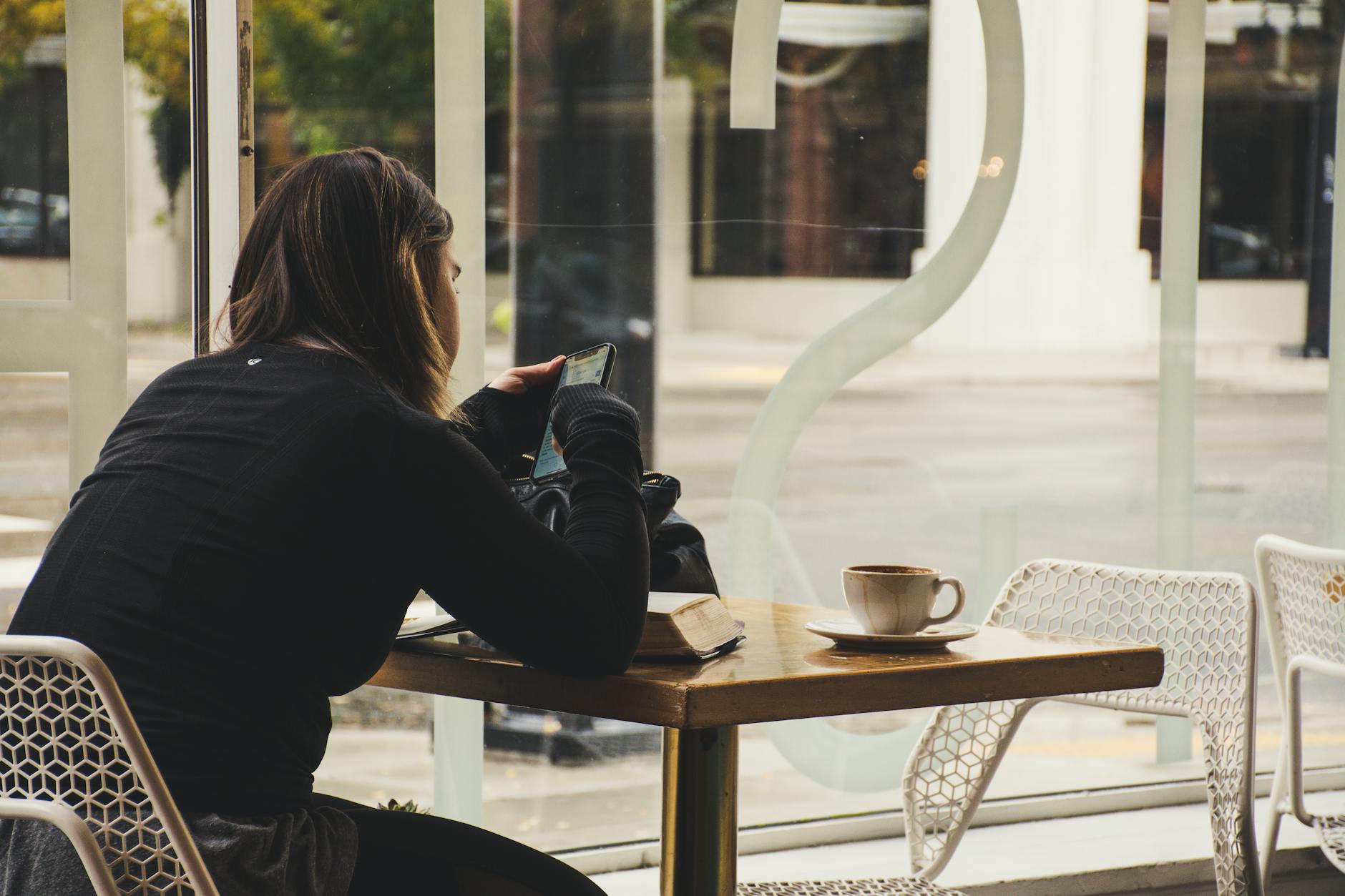 A woman enjoys coffee while using her smartphone at a cozy cafe table. - cbt for spring procrastination