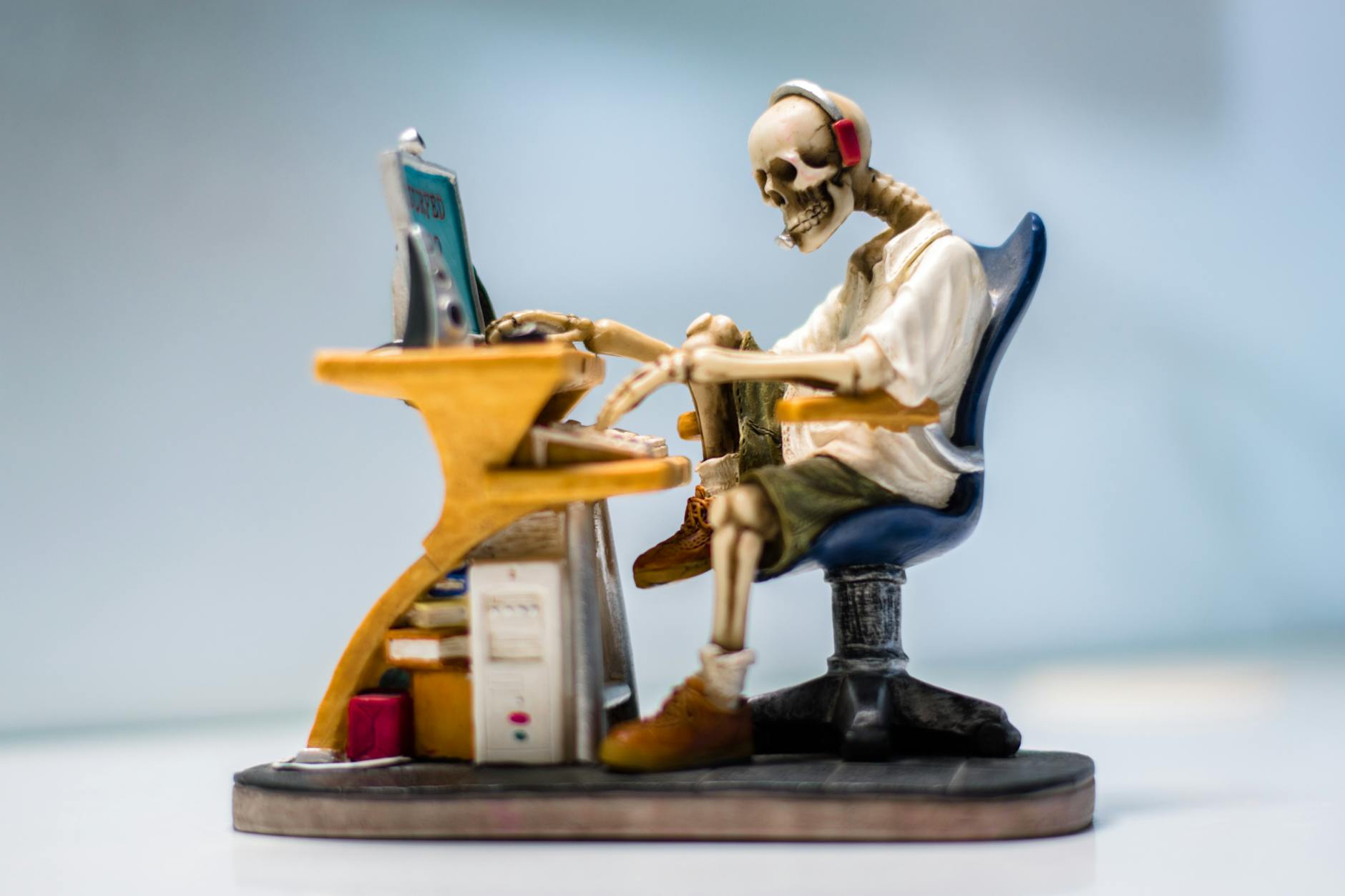 A quirky skeleton figurine wearing headphones sits at a desk with a computer, symbolizing burnout. - cbt for spring procrastination