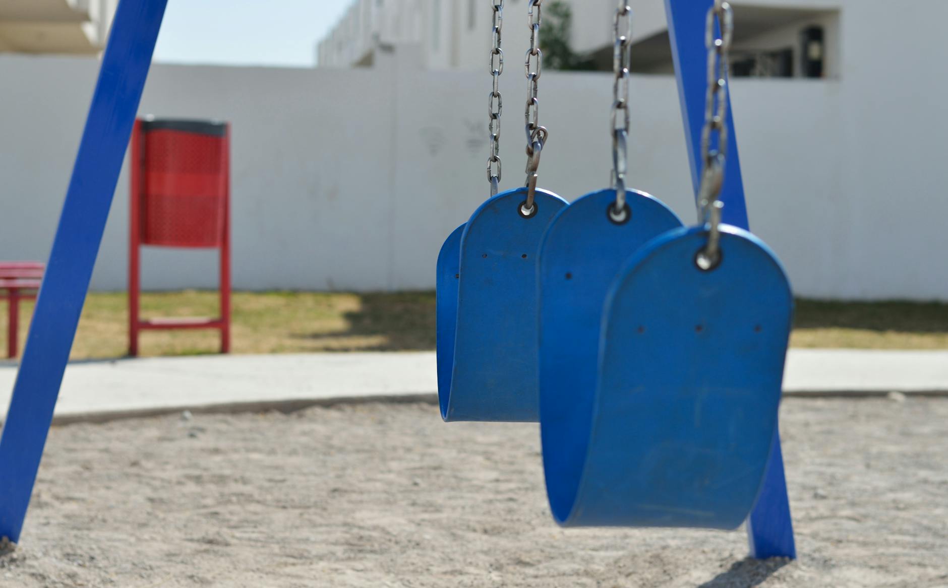 Blue swings in a sunny outdoor playground with sand and grass. - child allergy mood swings